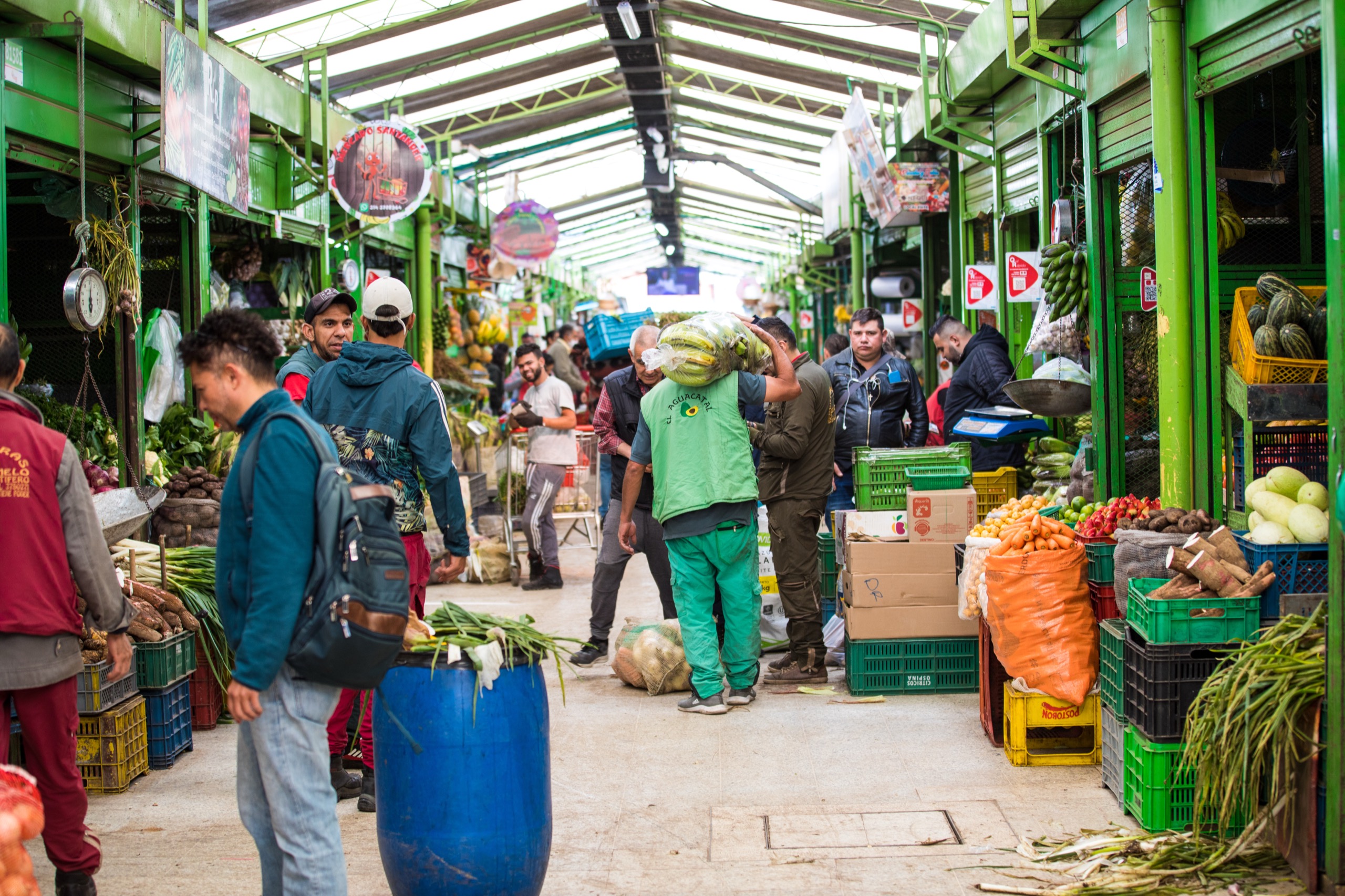 Vendors and shoppers move between stalls of fresh produce inside Bogotá's Paloquemao market hall.