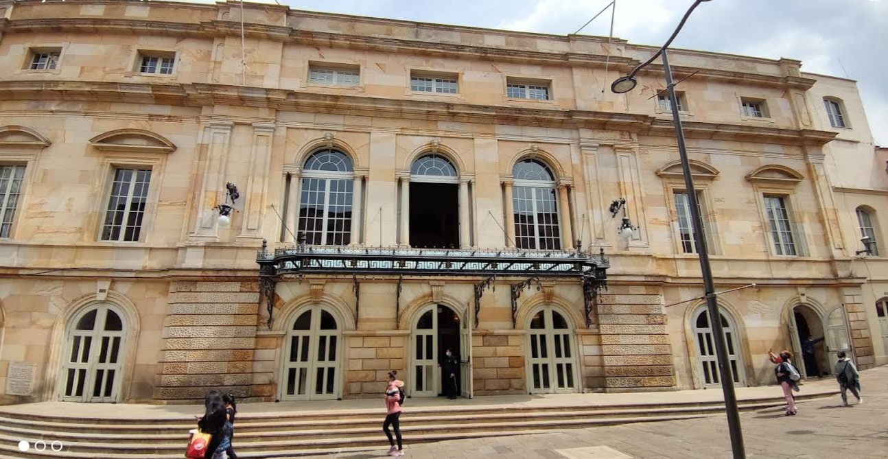 The sandstone facade, arched windows and iron balcony of a colonial-era building in downtown Bogotá, with visitors on the steps below.