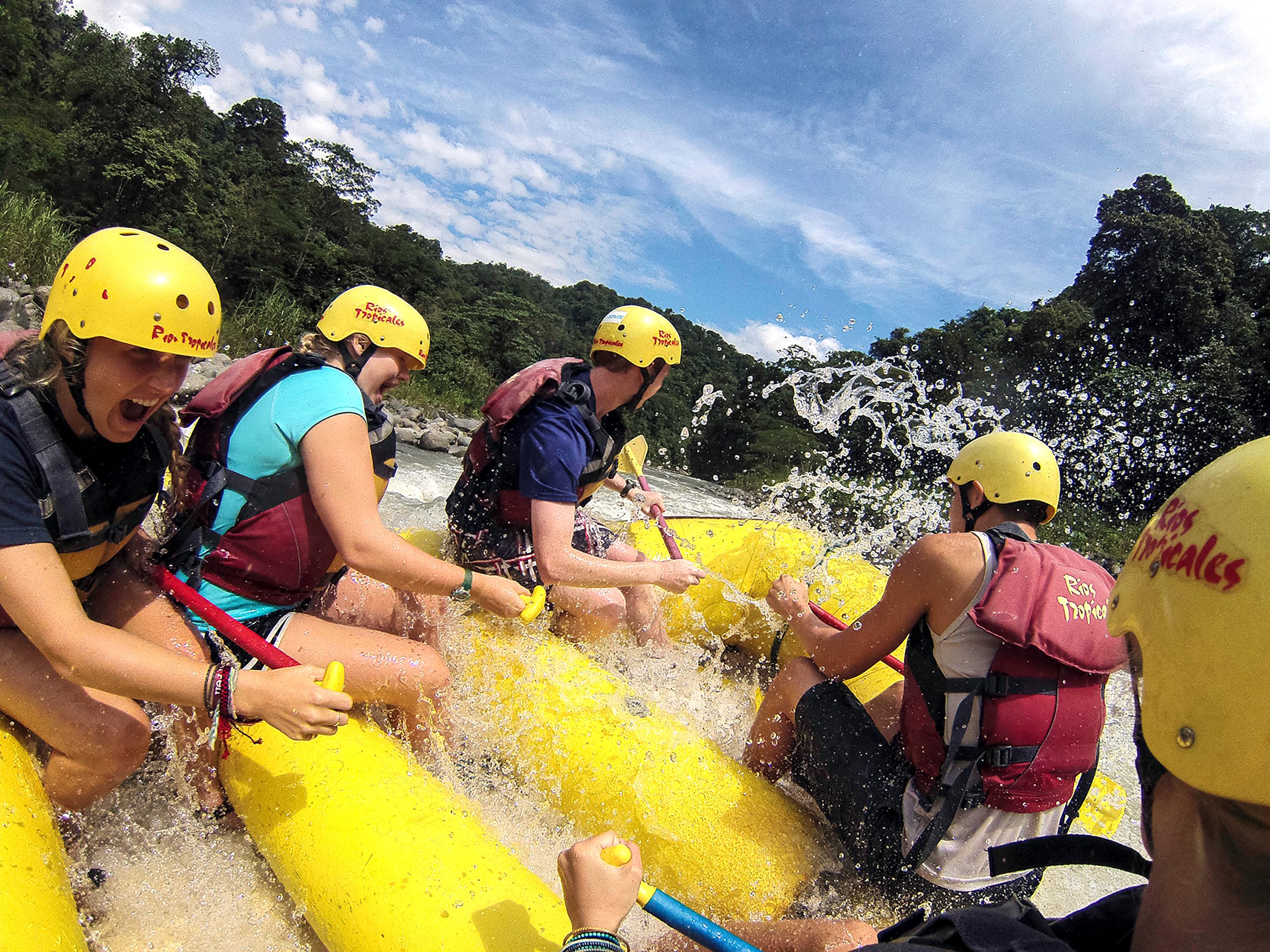 Students wearing helmets and life jackets rafting down a river, demonstrating Rustic Pathways’ student travel emergency protocols and outdoor adventure safety measures.