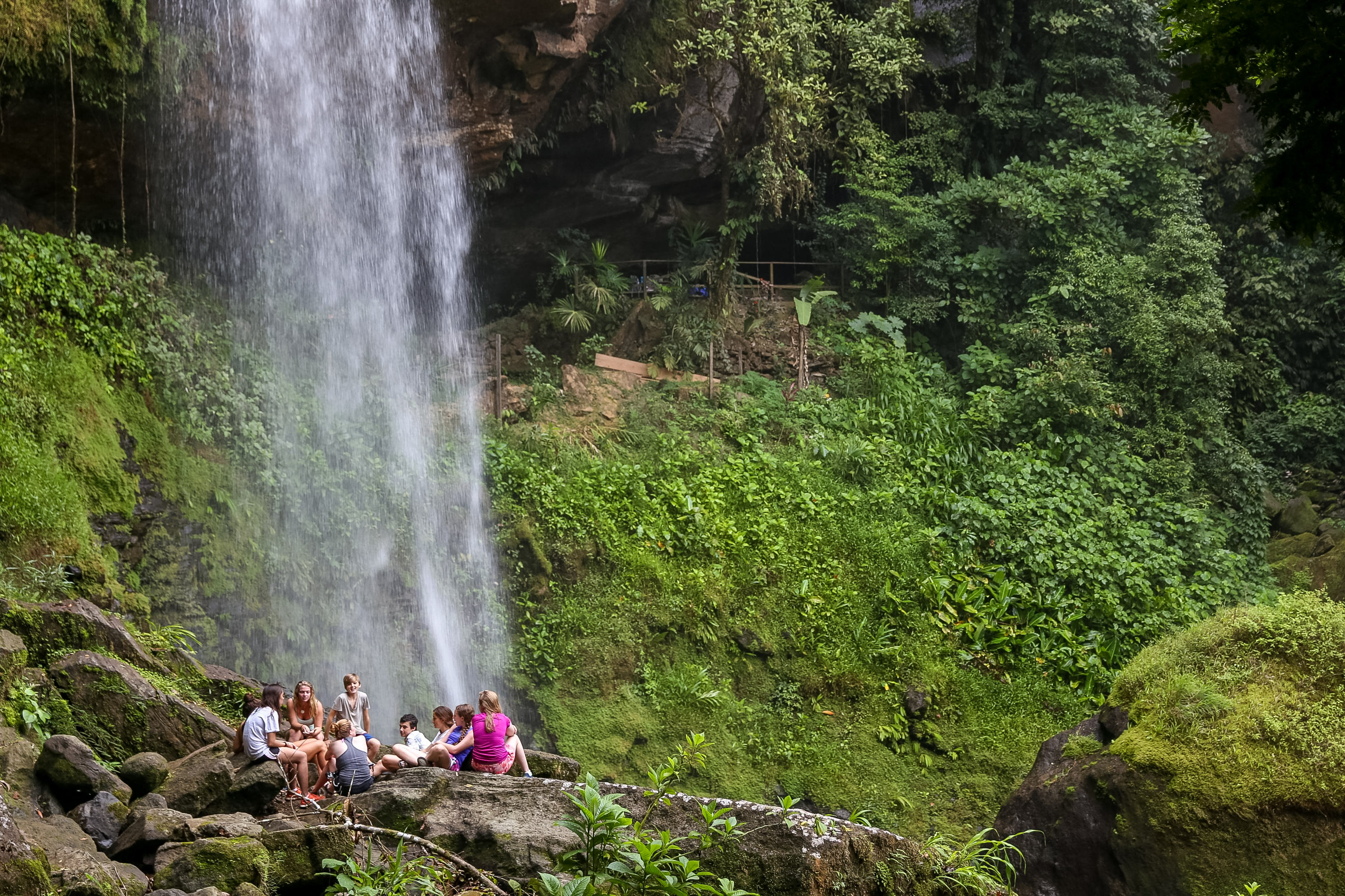 Students gather on rocks at the base of a jungle waterfall