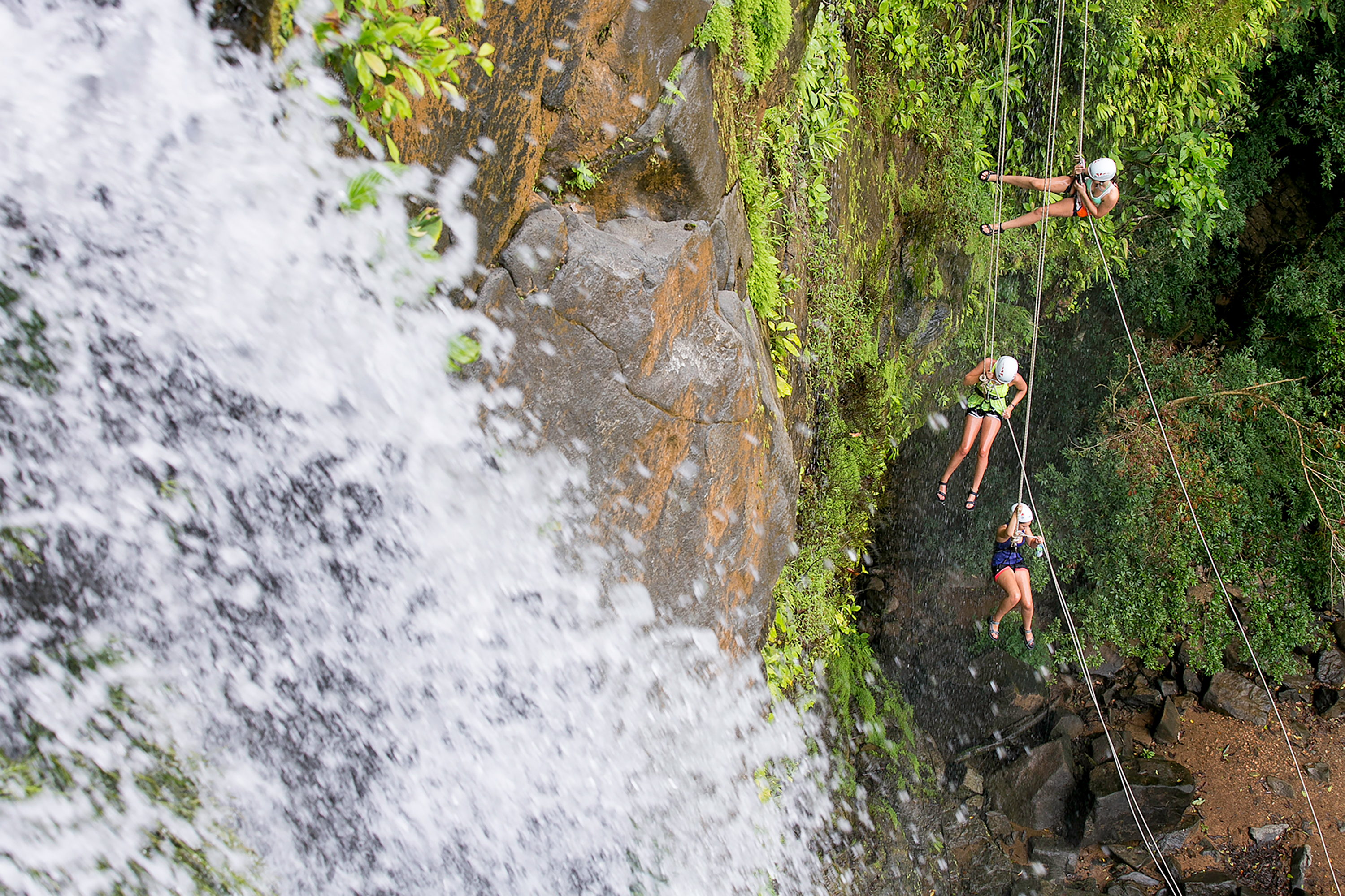Students rappel down a rocky cliff beside a rushing waterfall in Costa Rica