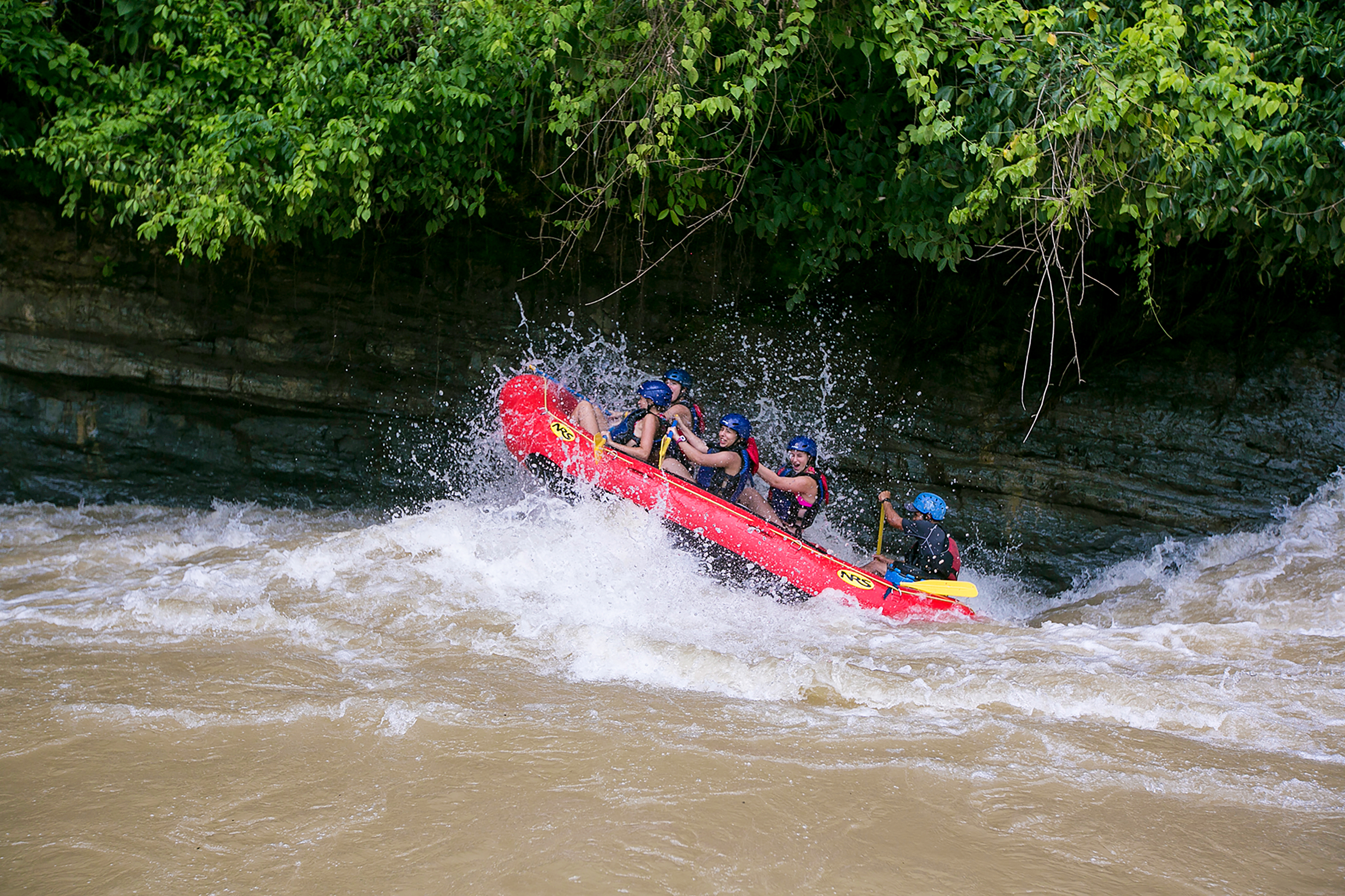 Teen travelers in helmets raft through whitewater on a jungle river