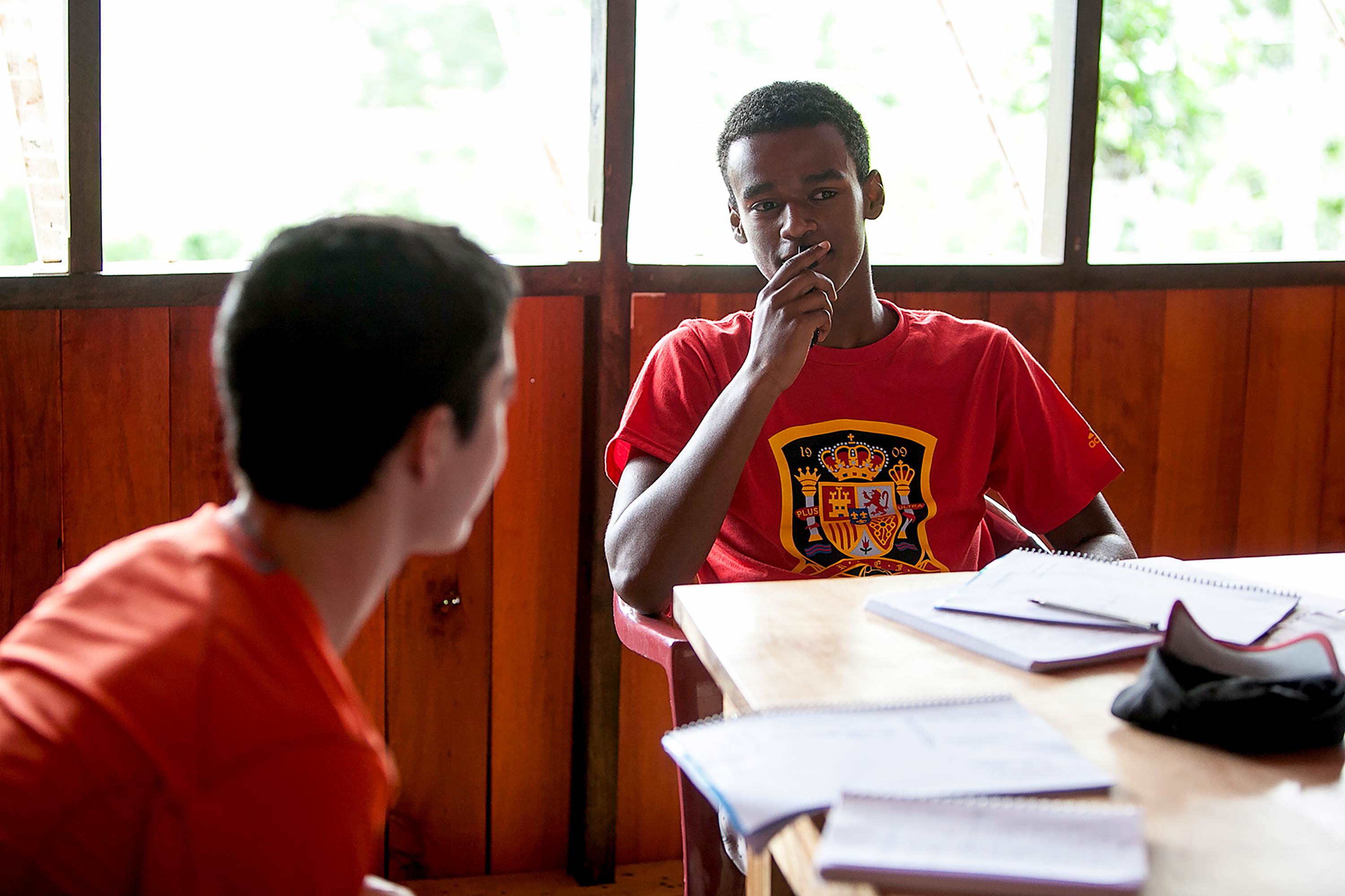 Two students at a desk with open workbooks in a wooden classroom