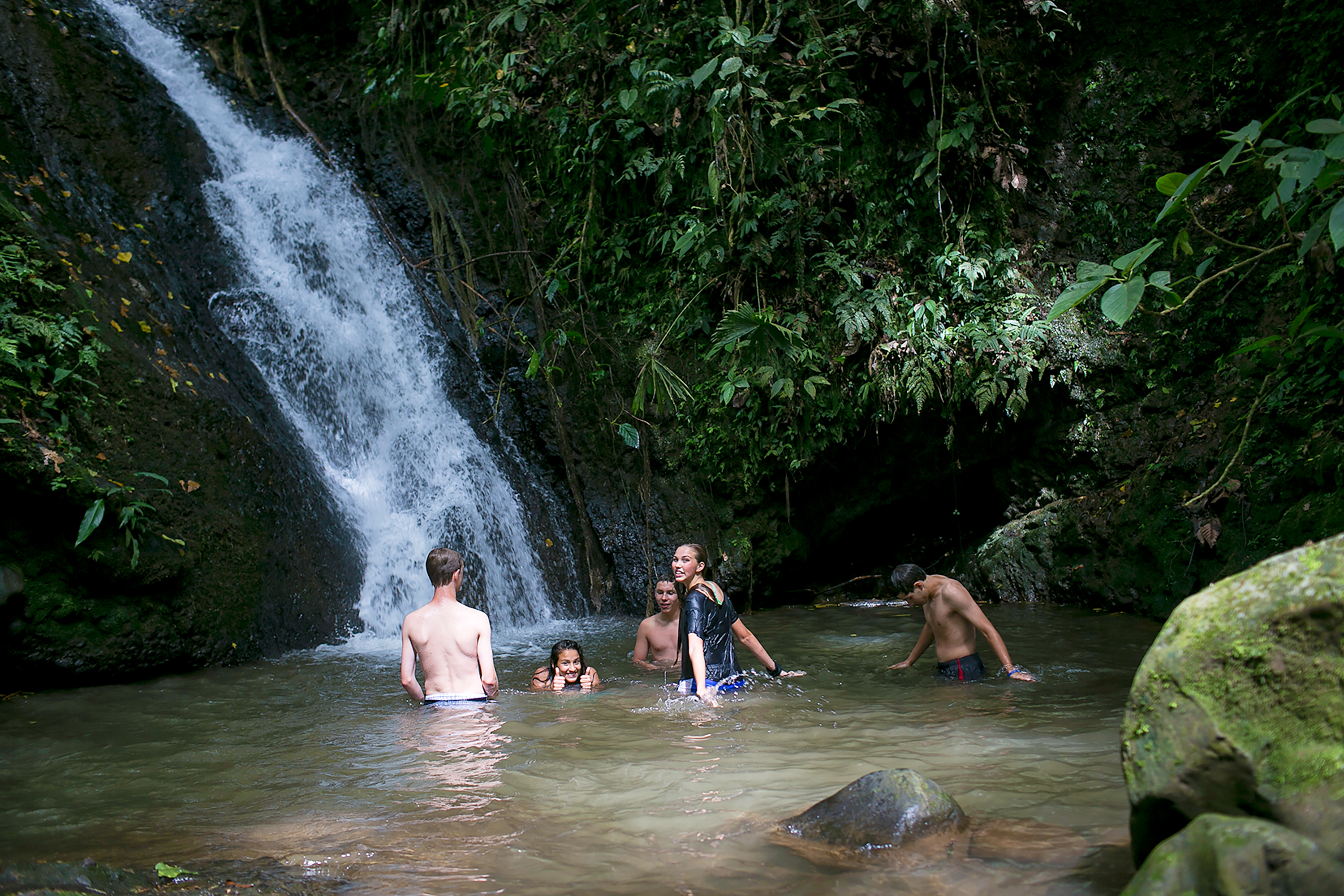 Students swimming in the pool beneath a rainforest waterfall