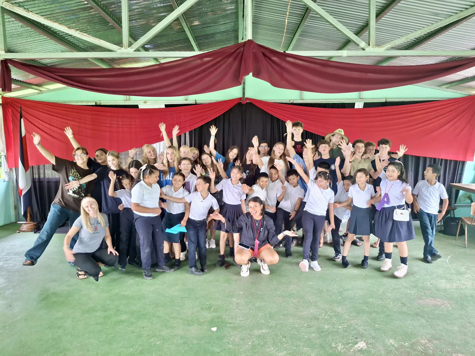 A Rustic Pathways group and a class of Costa Rican schoolchildren with their arms raised under a pavilion