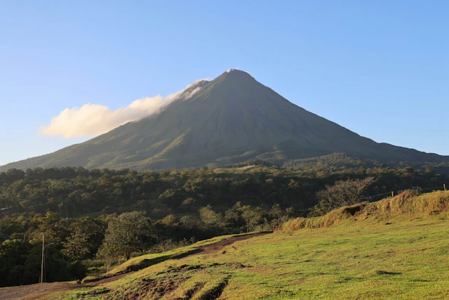 Arenal Volcano rises above rainforest and green pasture near La Fortuna, Costa Rica
