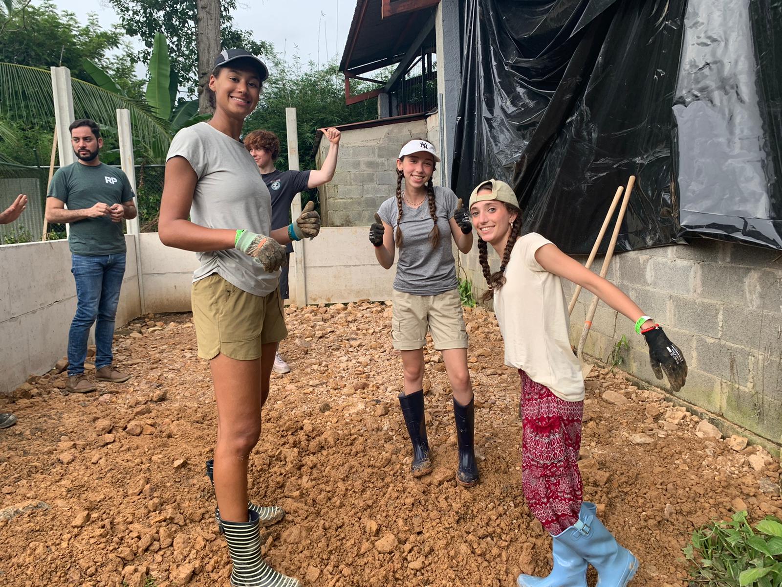 Students give a thumbs-up while working on a dirt construction site during a community service project