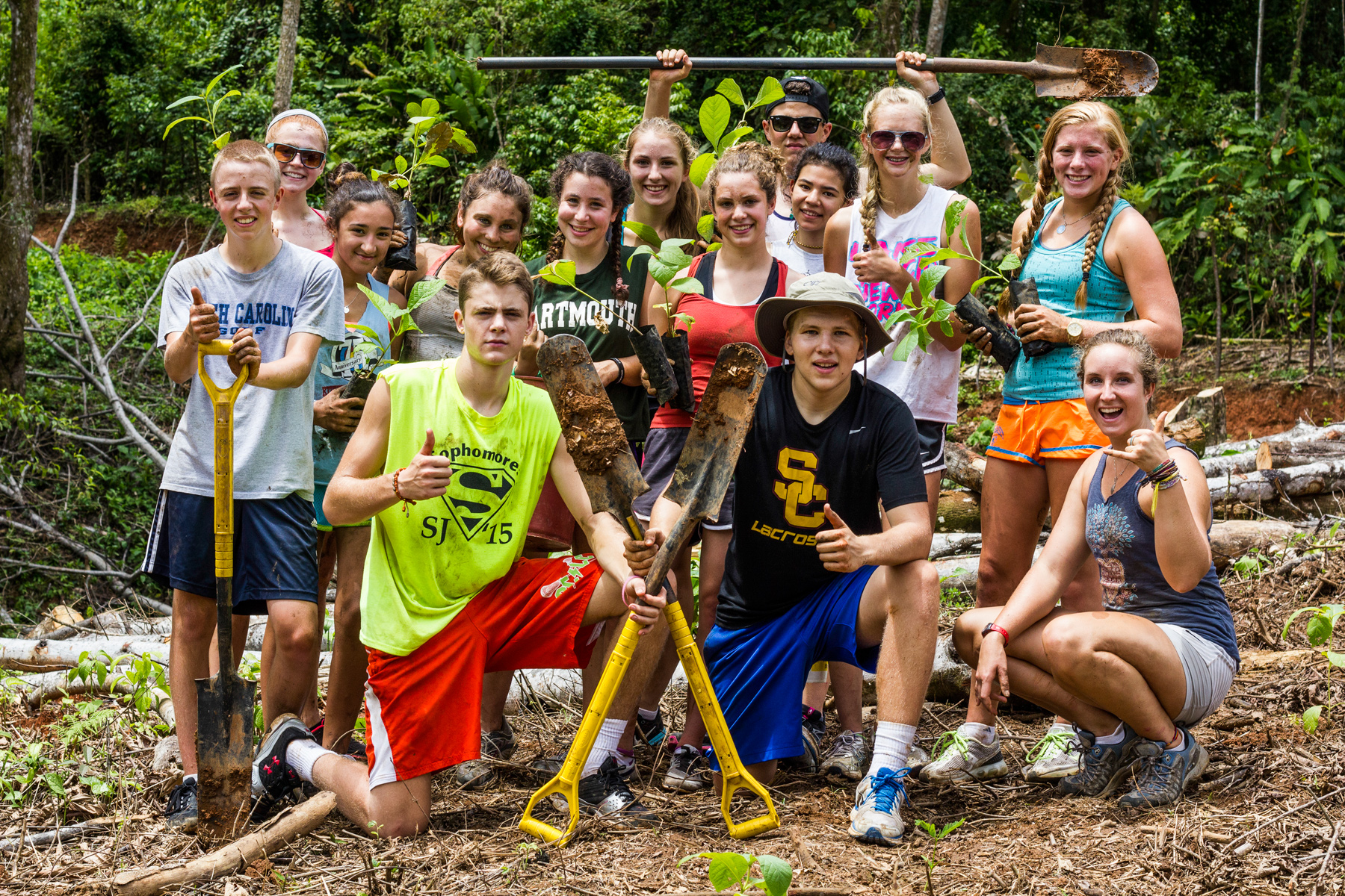 Students pose with shovels and saplings after a tree-planting service project in a cleared forest area
