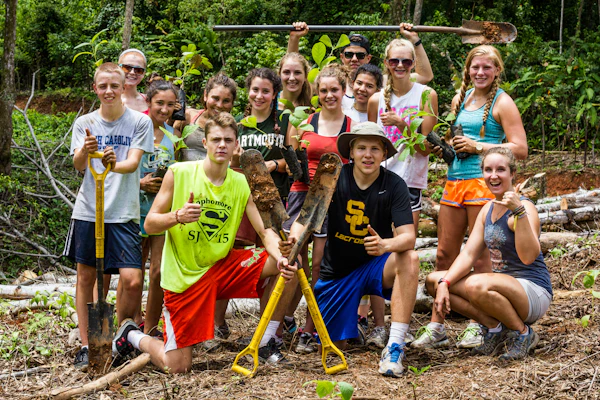 A school group stands together with rakes and tools at the start of a service day
