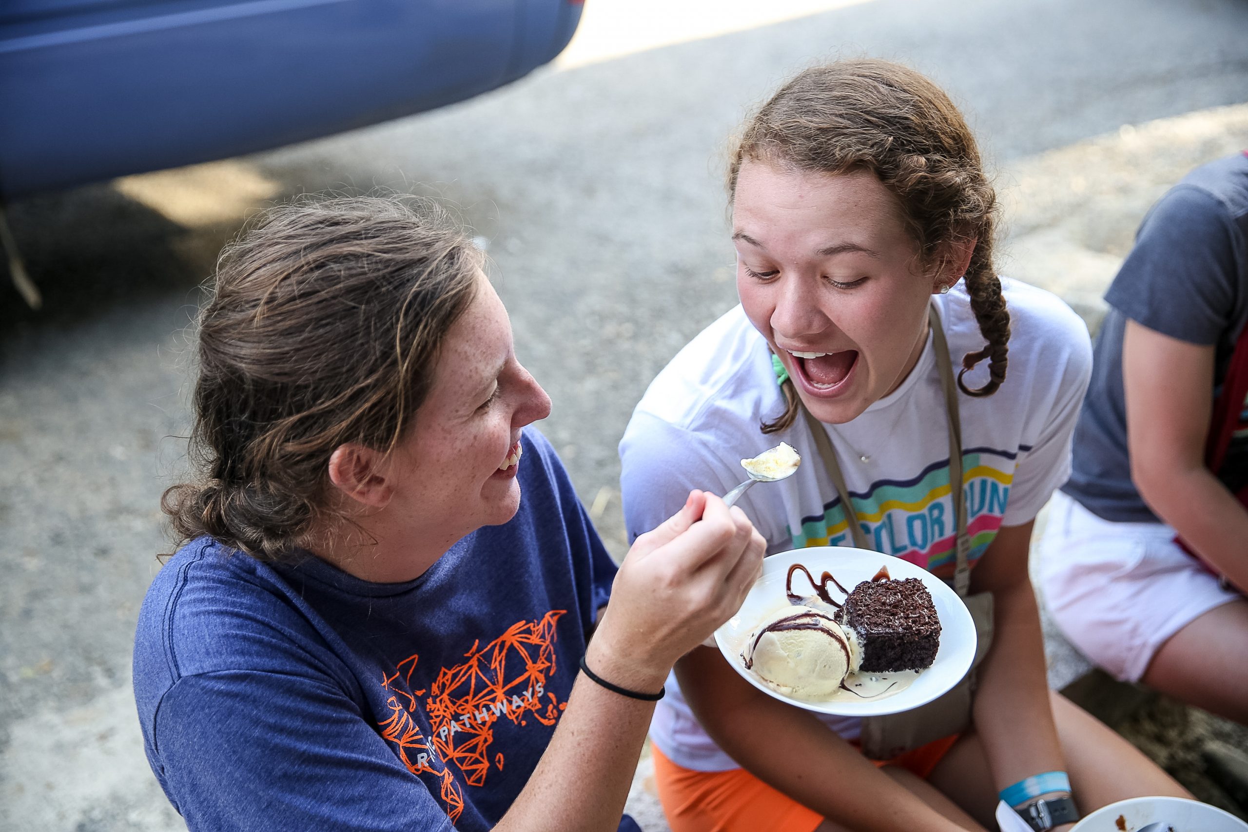 A student laughs while being fed a bite of dessert