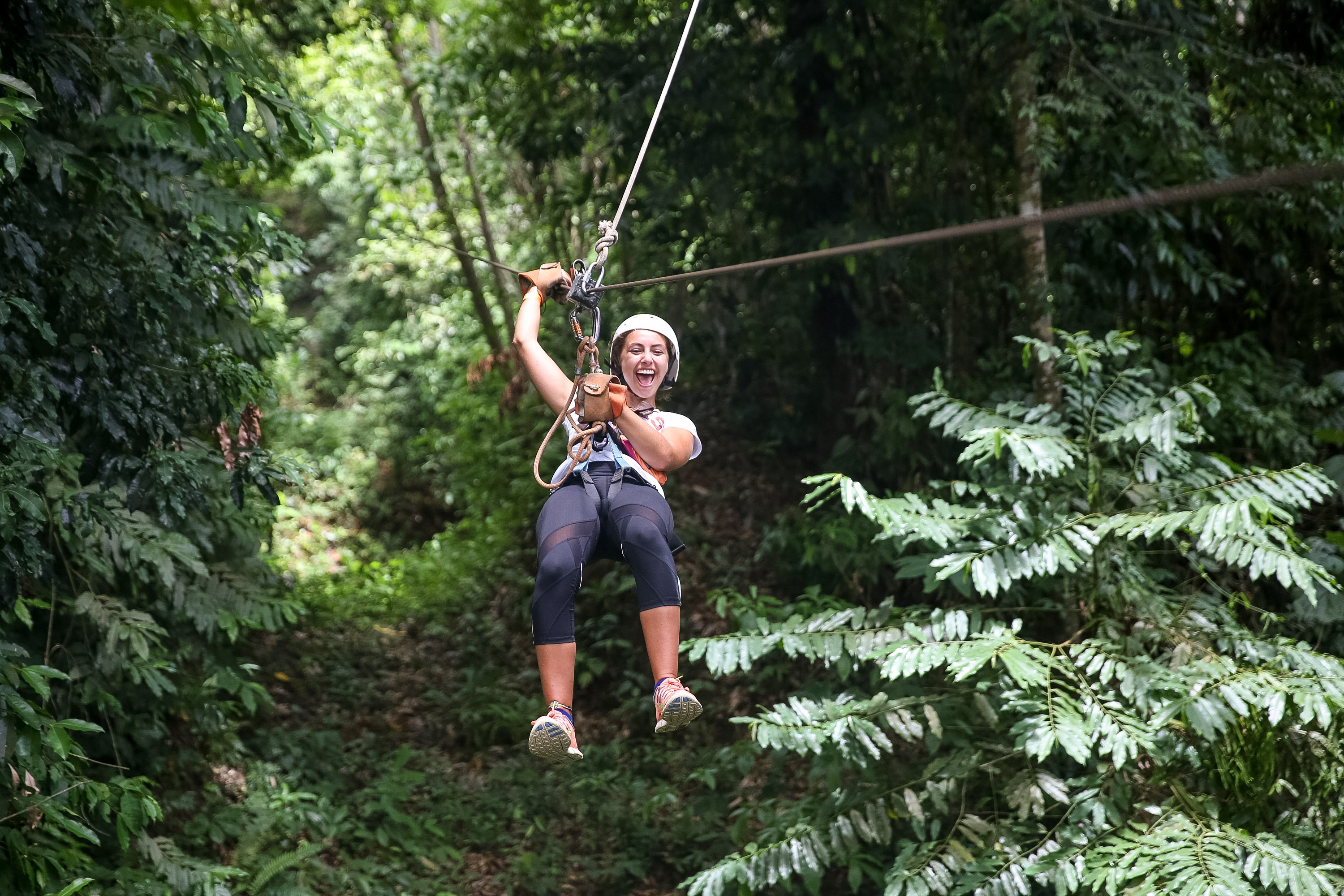 A student ziplines through the jungle canopy, laughing