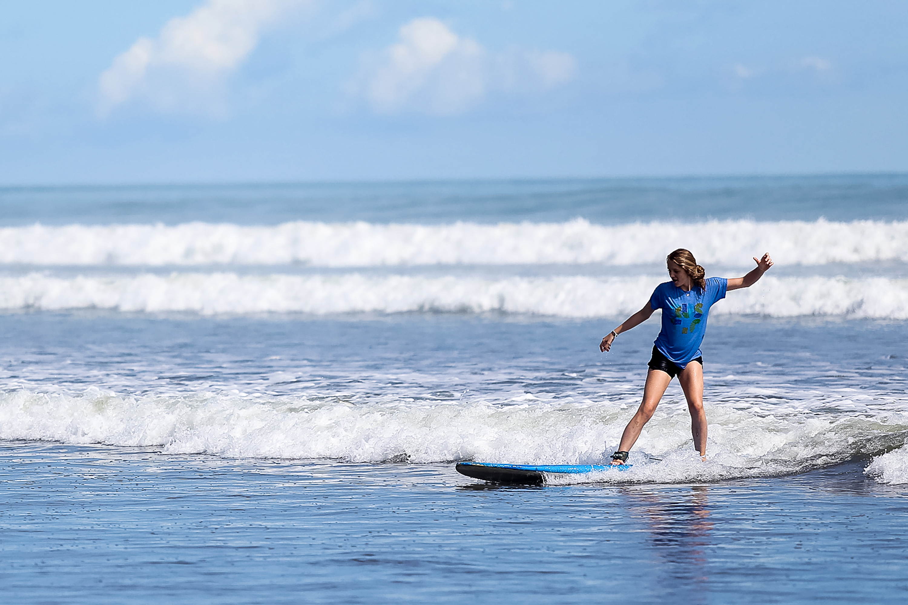 A student balances on a surfboard while riding a wave to shore