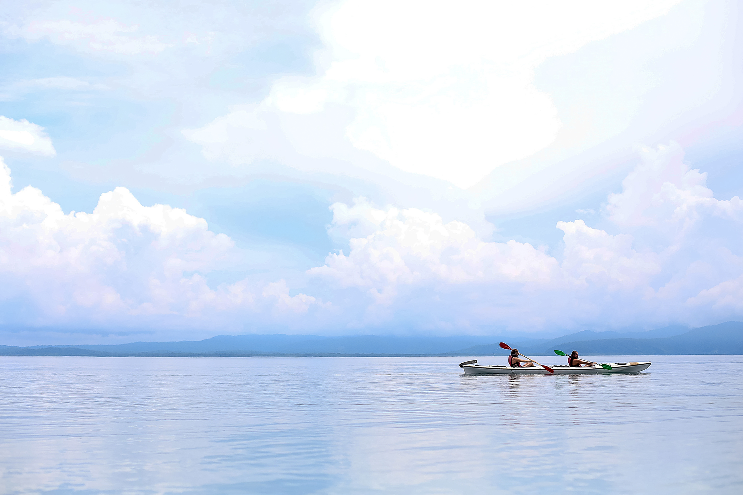 Students paddle a kayak across calm open water under a cloudy sky