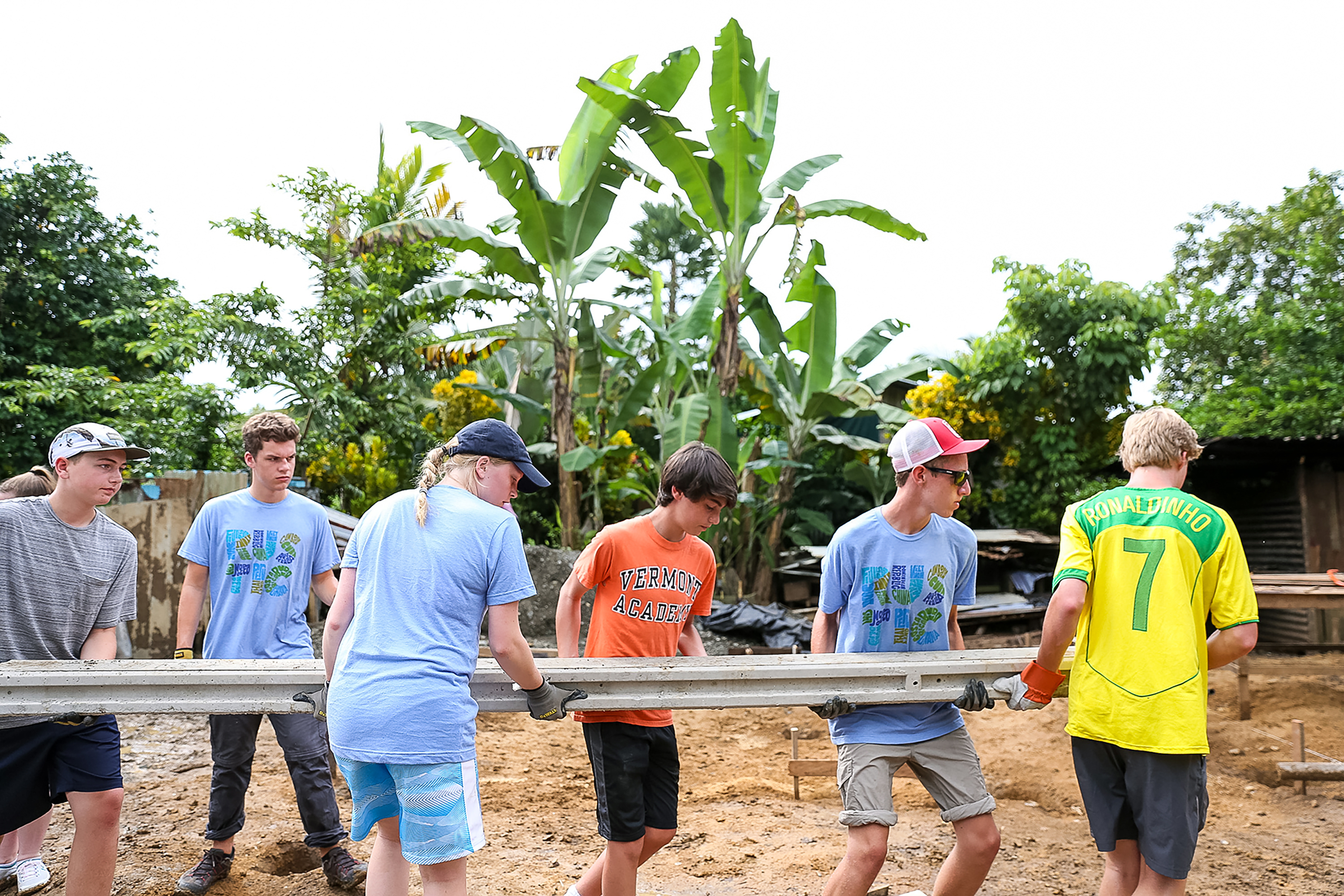Students carry a metal beam together at a construction service site