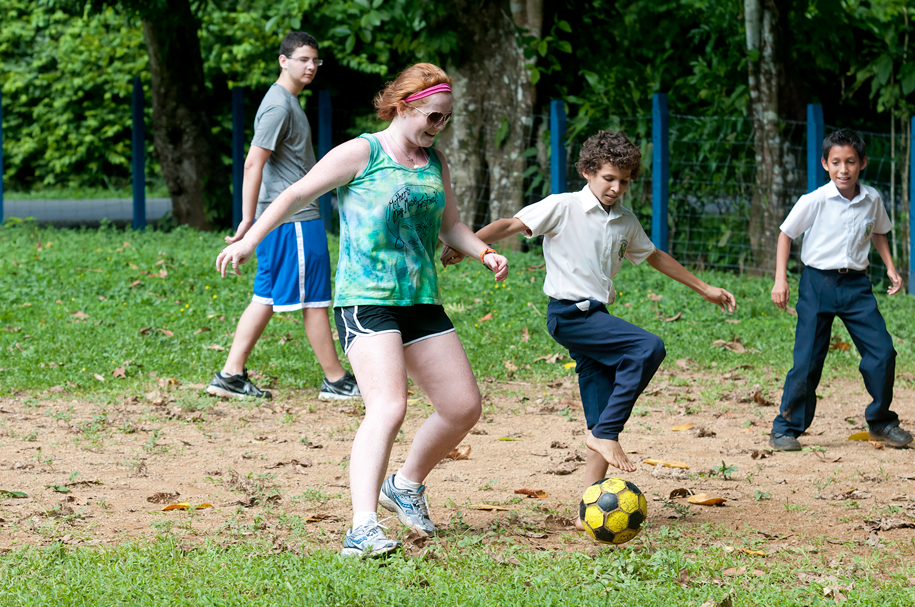 A student plays soccer with local kids on a dirt field near the jungle