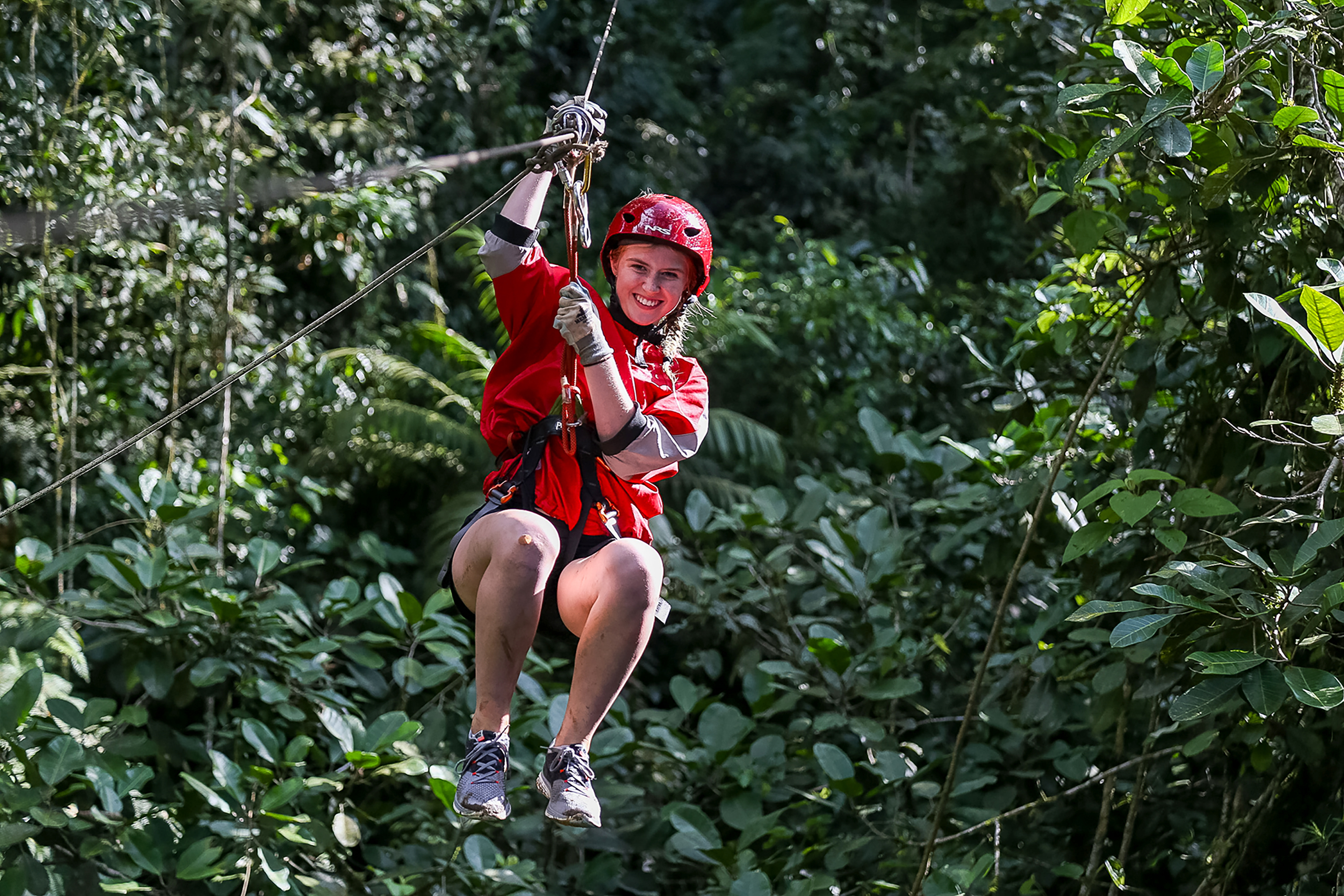 Student riding a zipline through the forest canopy in a helmet and harness
