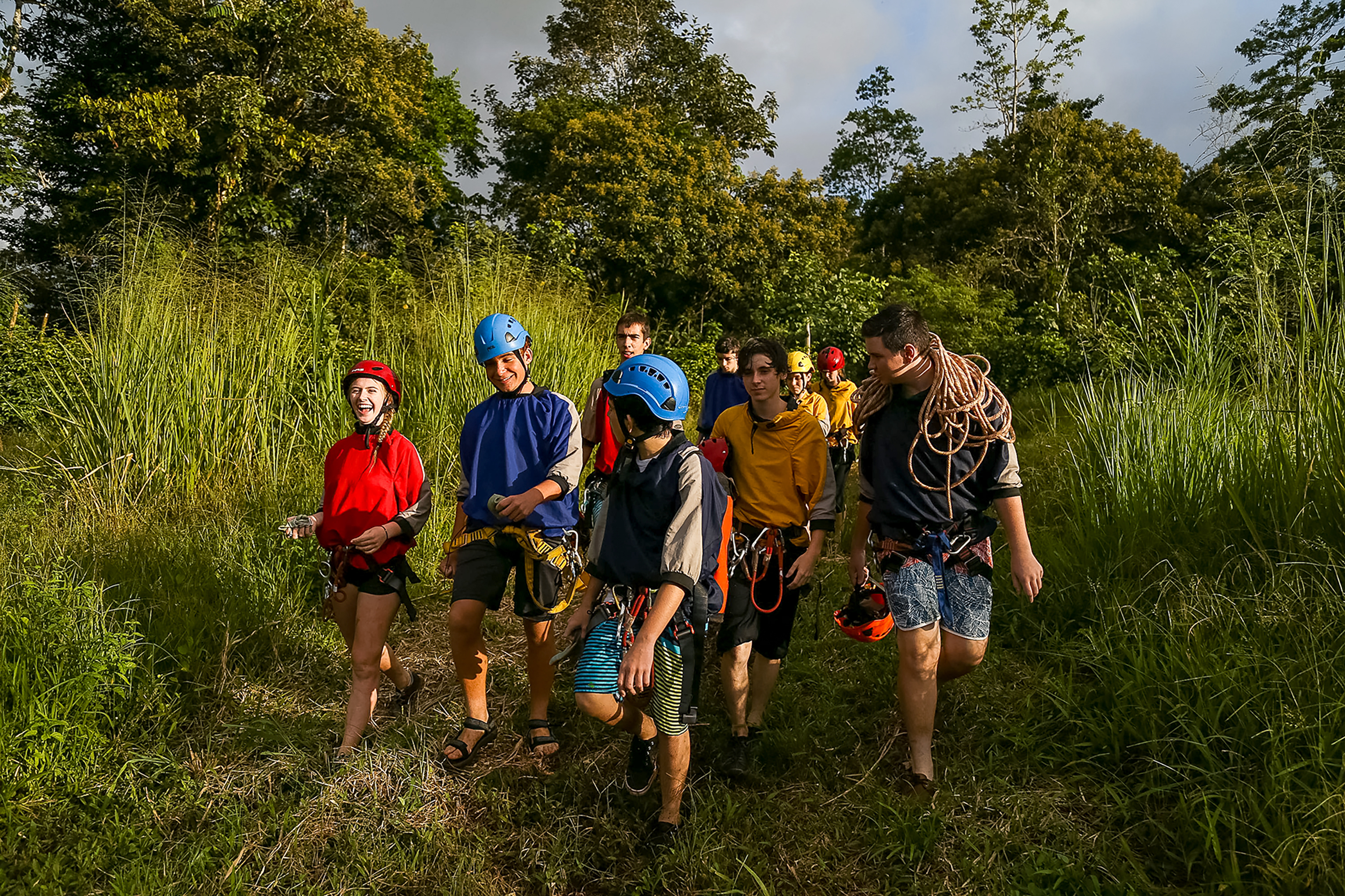 Students in helmets and harnesses walking single file through tall grass
