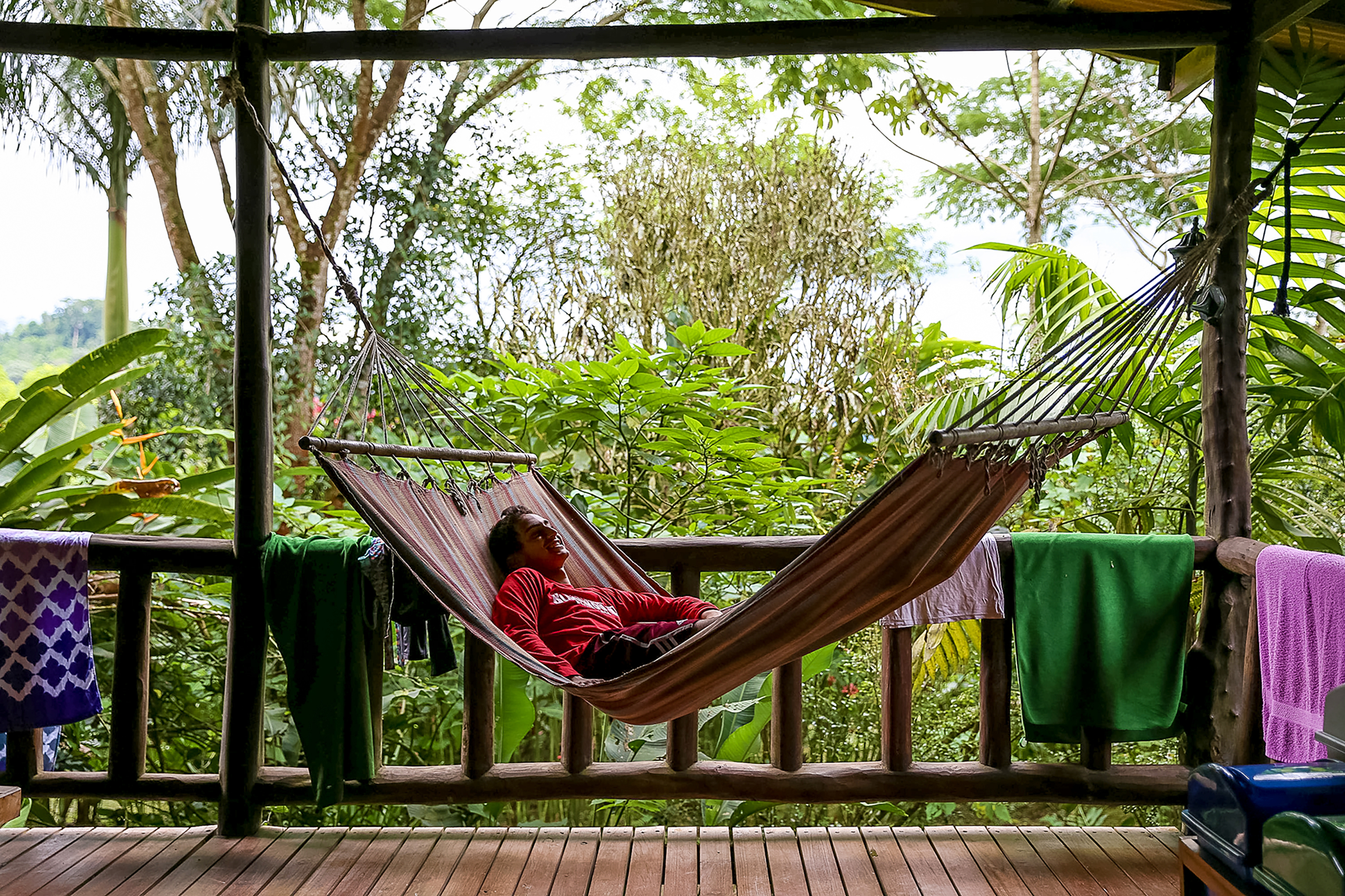 A student relaxes in a hammock on a covered porch surrounded by jungle greenery