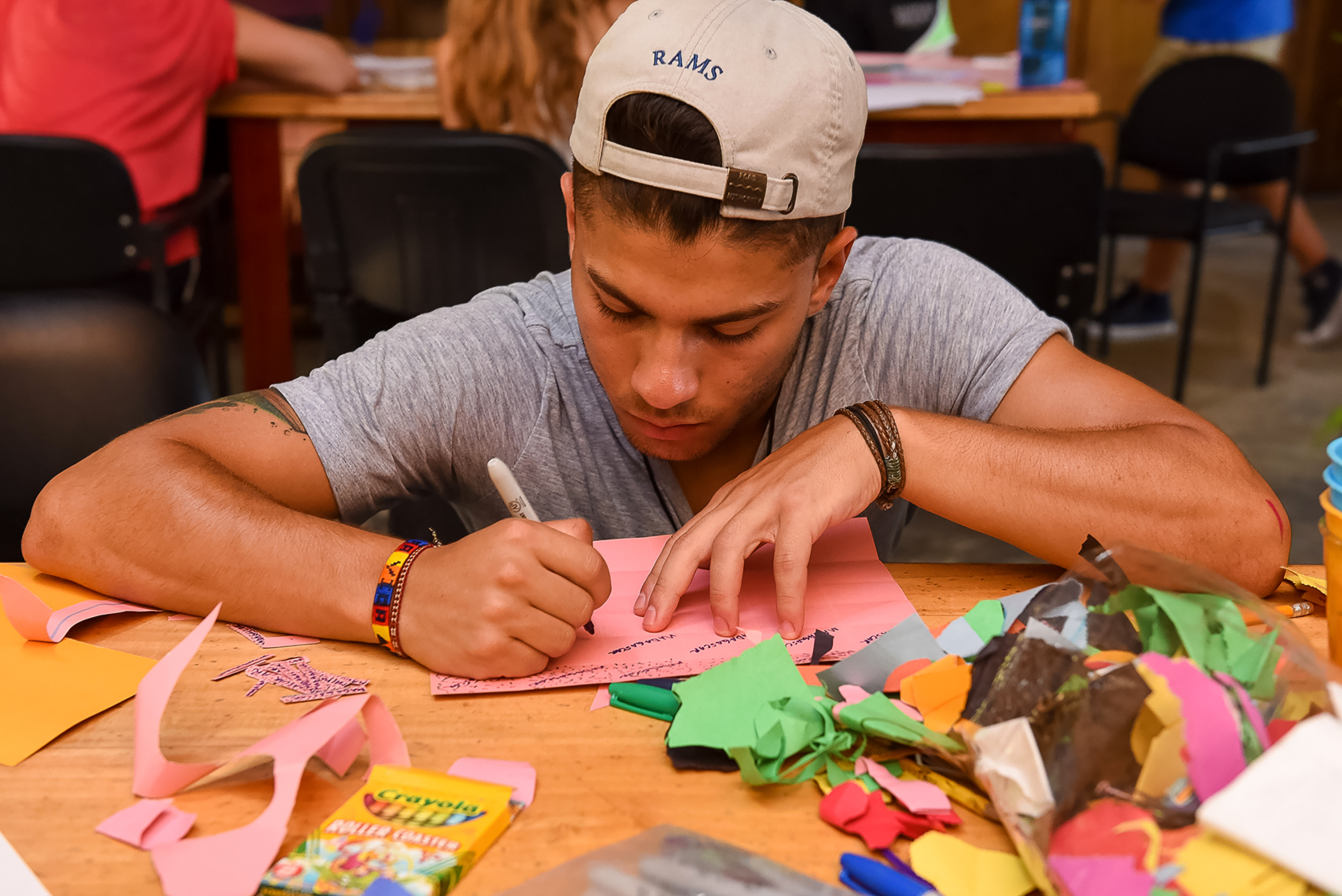 A student concentrates on a craft project surrounded by colorful paper scraps