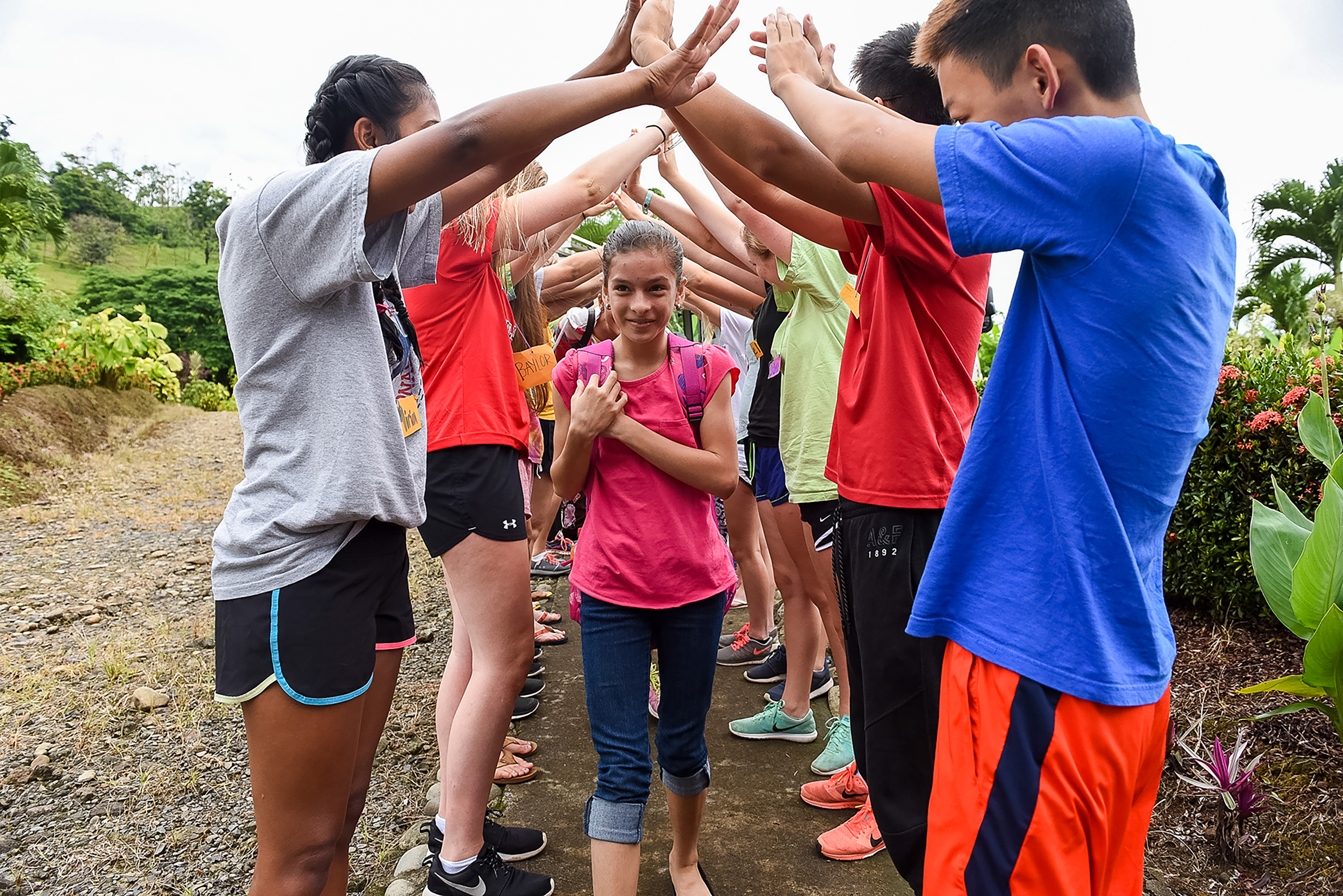 A student in Costa Rica walks through a tunnel of high-fives from her group on a gravel path
