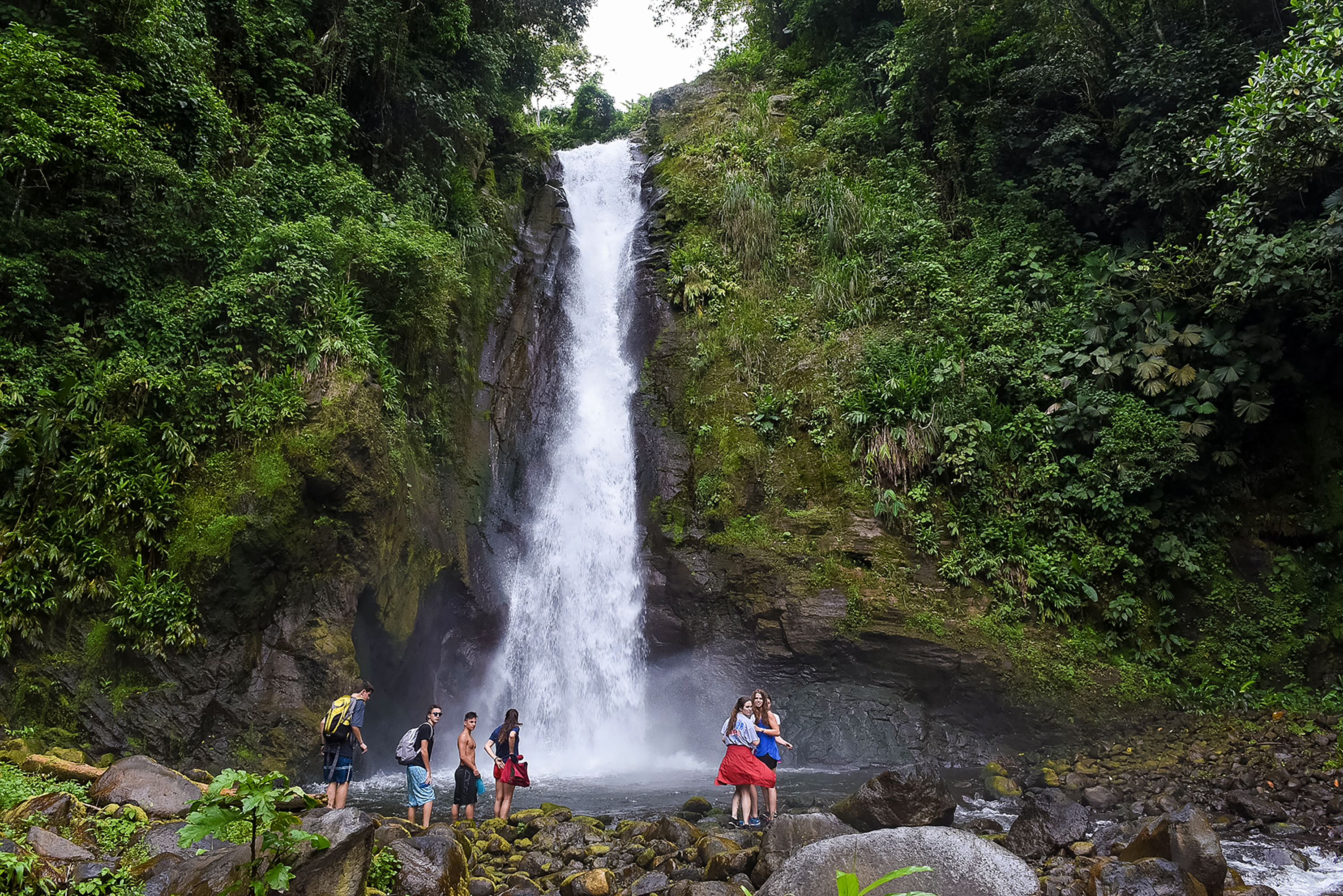 Students standing at the base of a tall waterfall