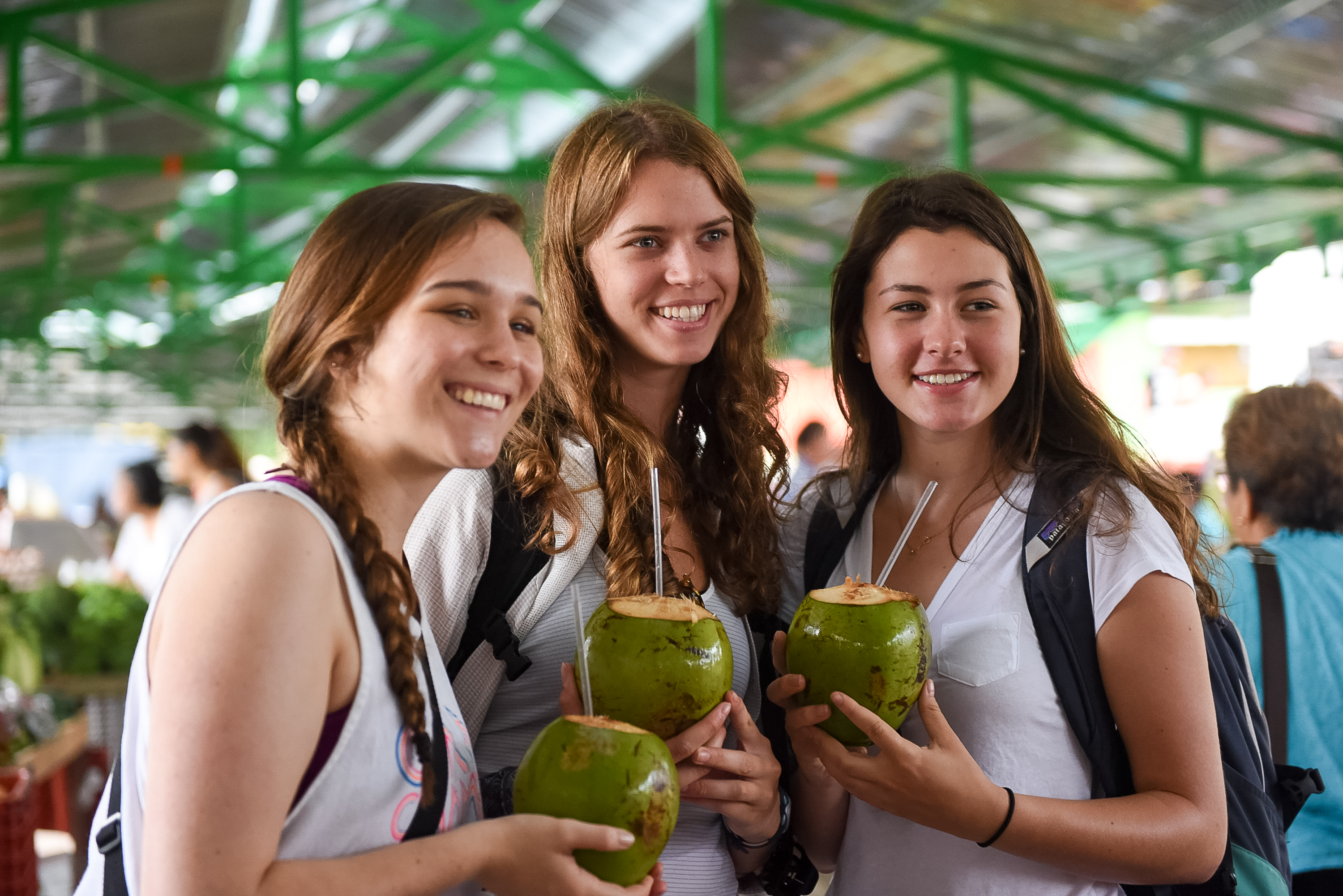 Three students holding fresh green coconuts with drinking straws
