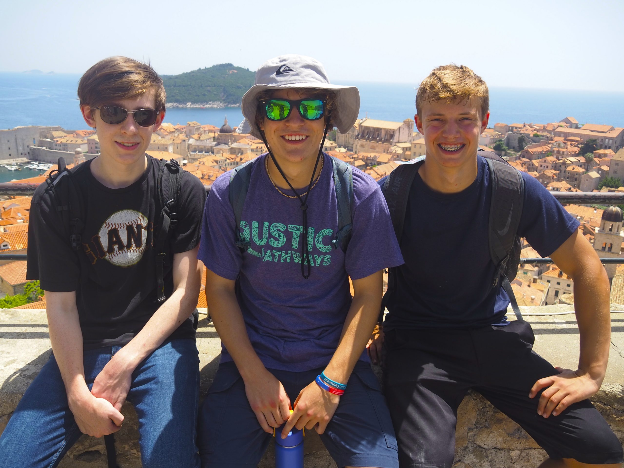 Students smile atop a stone wall overlooking Dubrovnik's terracotta rooftops and the sea