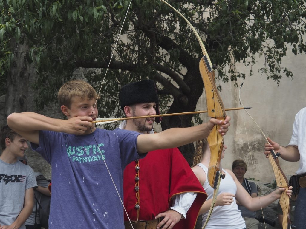 A student wearing a Rustic Pathways student shoots a bow during a cultural activity on a summer program in Croatia for high school students.