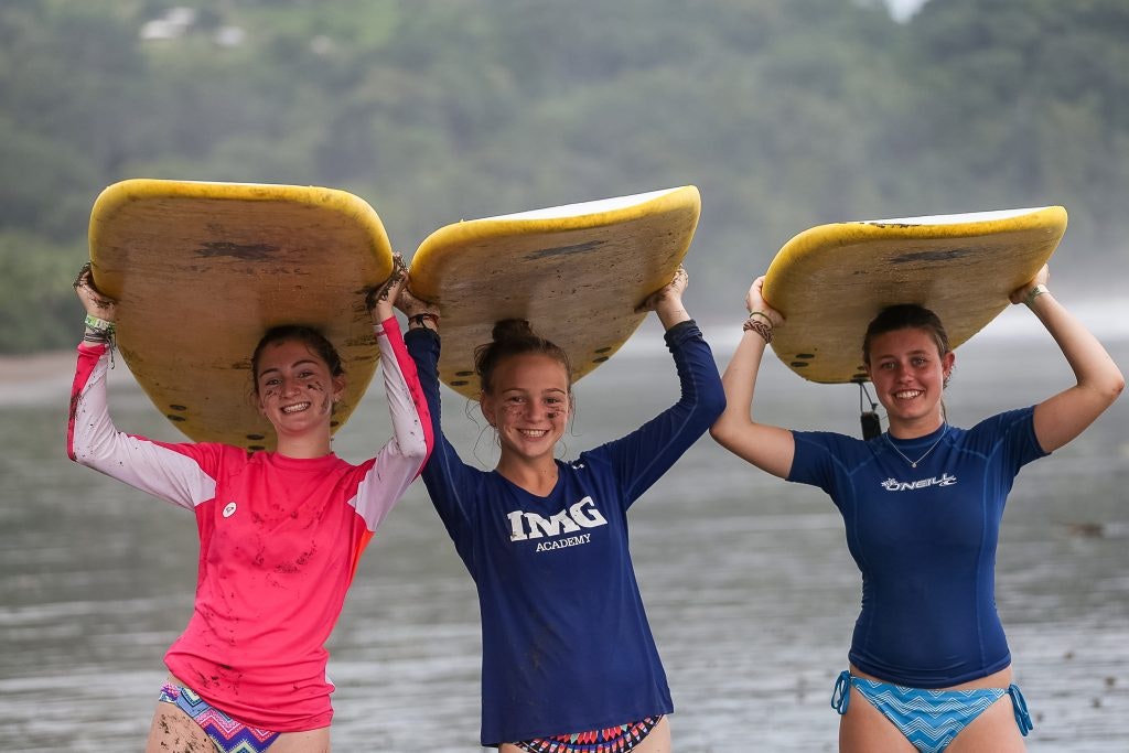 Three teen travelers holding surfboards above their head before a surf lesson in Costa Rica during a spring break teen tour.