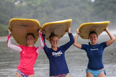 Three teen travelers holding surfboards above their head before a surf lesson in Costa Rica during a spring break teen tour.