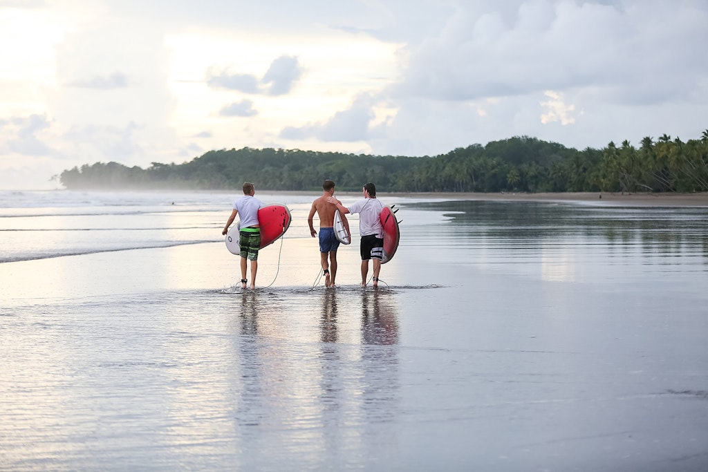 Teens walking with surfboards on a tropical beach during Rustic Pathways summer volunteer abroad programs in Costa Rica