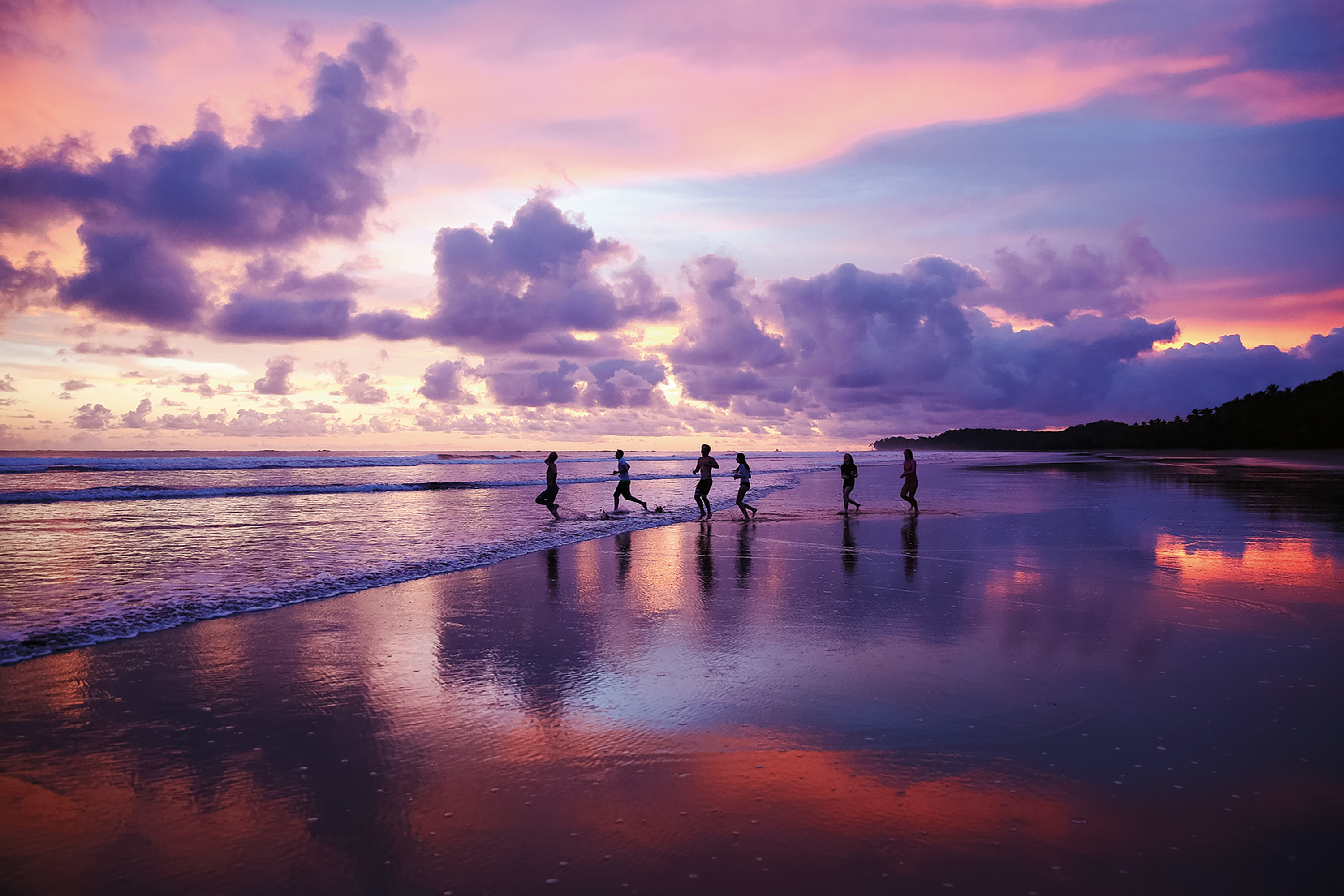 Picture of a sunset in the beach with 6 people walking along the coast.