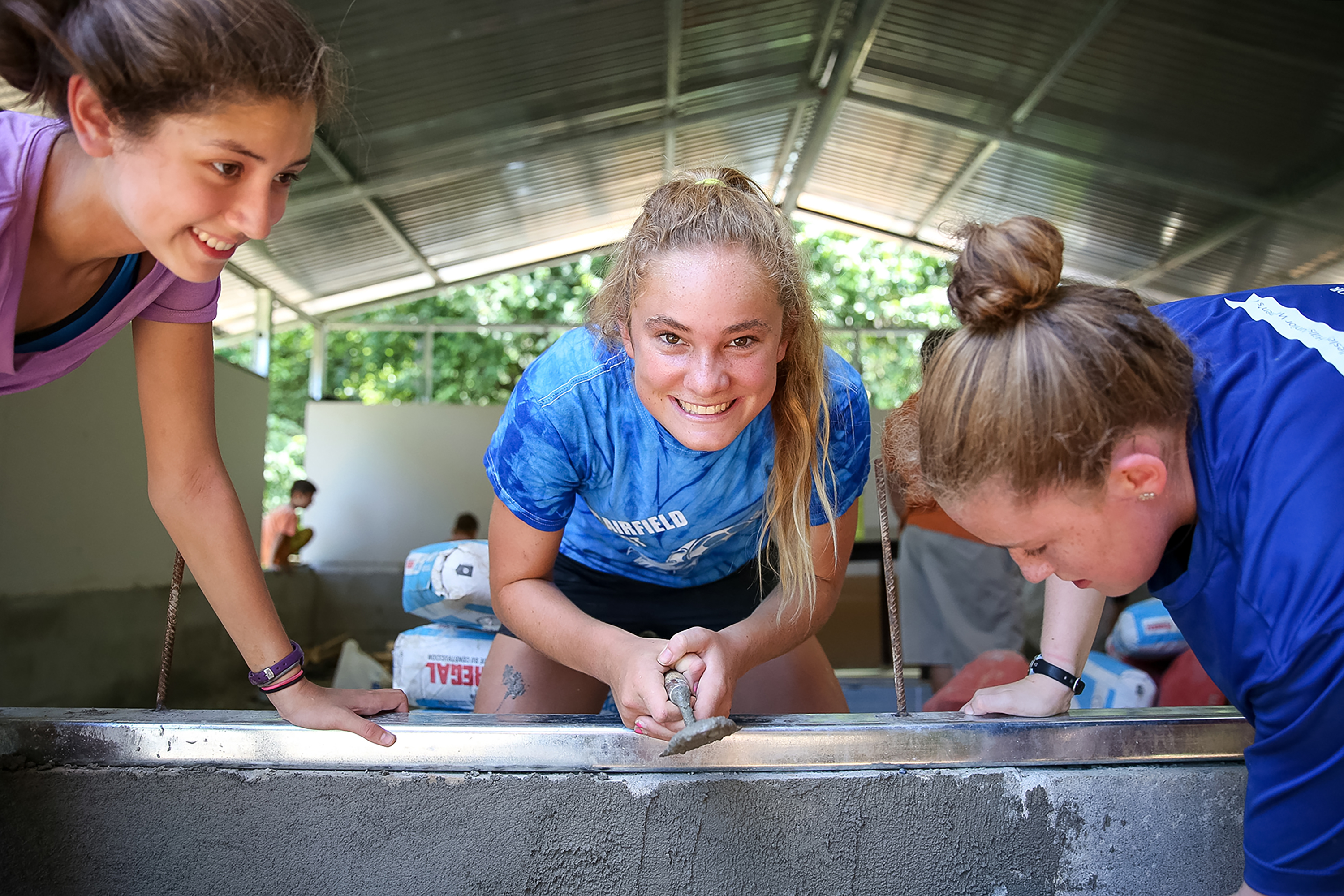 Picture of three girls doing service projects (paving cement).