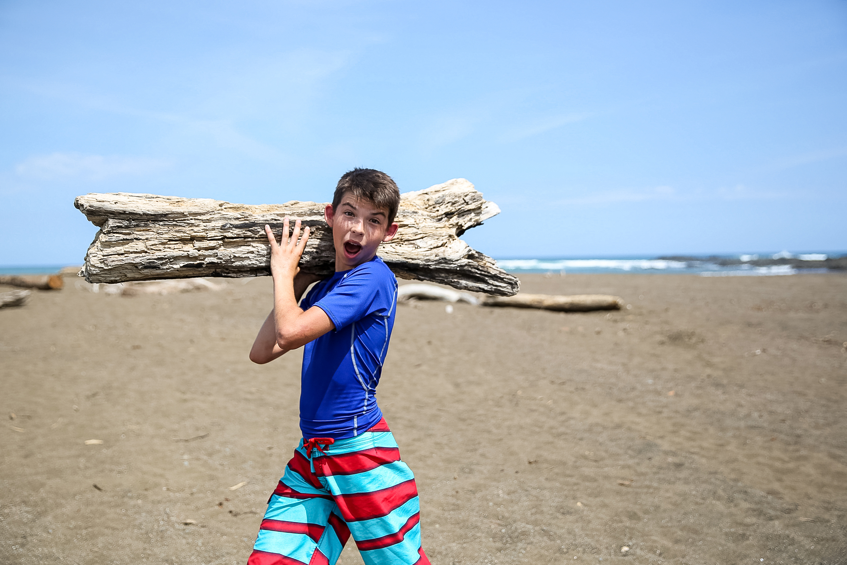 Picture of boy carrying a log on his shoulder at the beach.