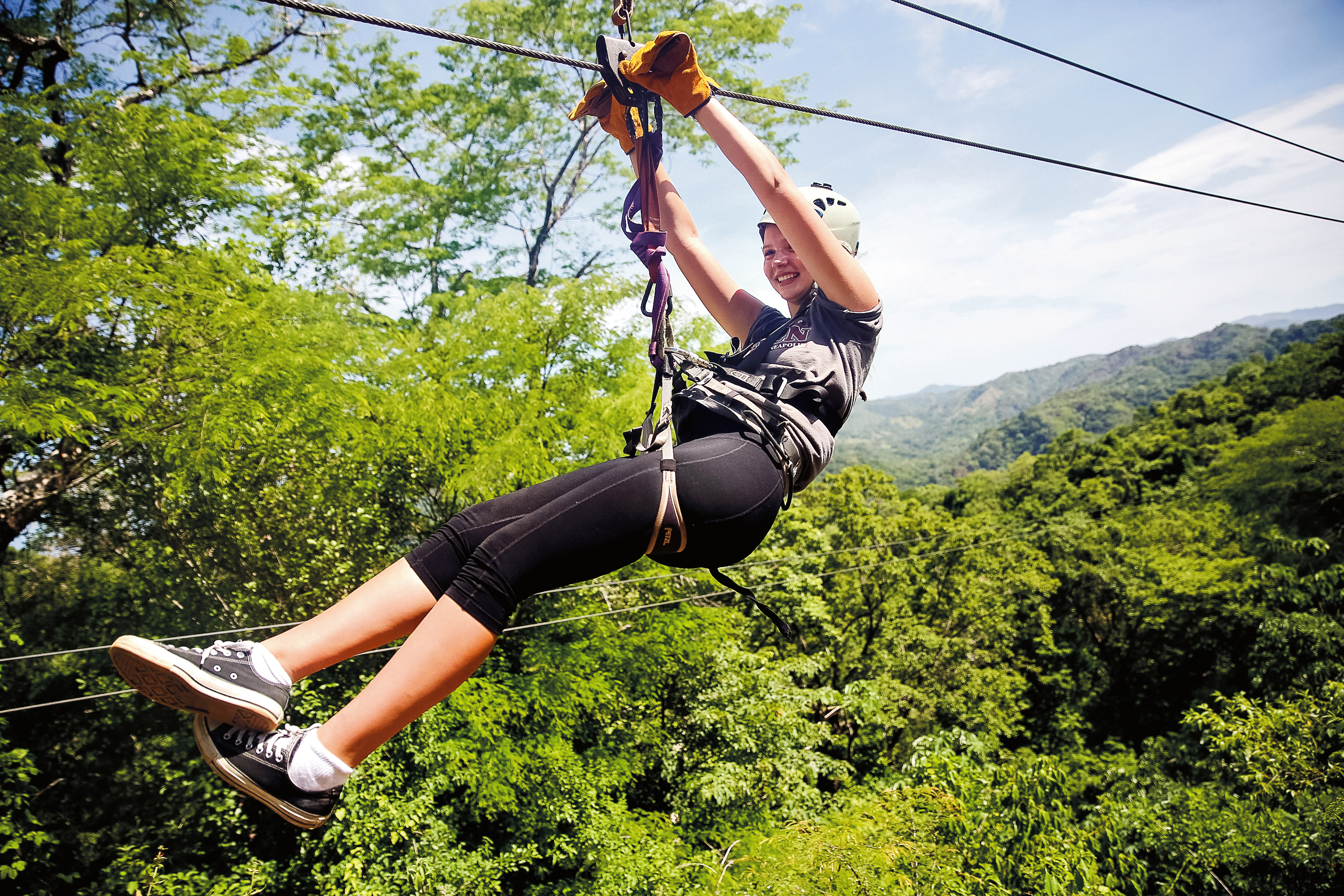 A student ziplines above a lush forest canopy
