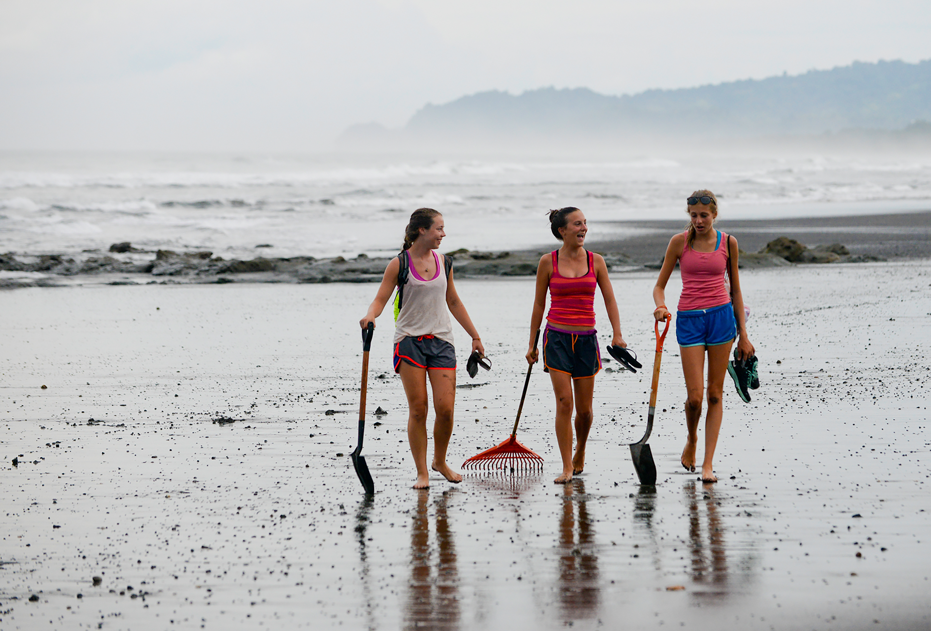 Picture of students carrying shovels and rake while walking on the beach.