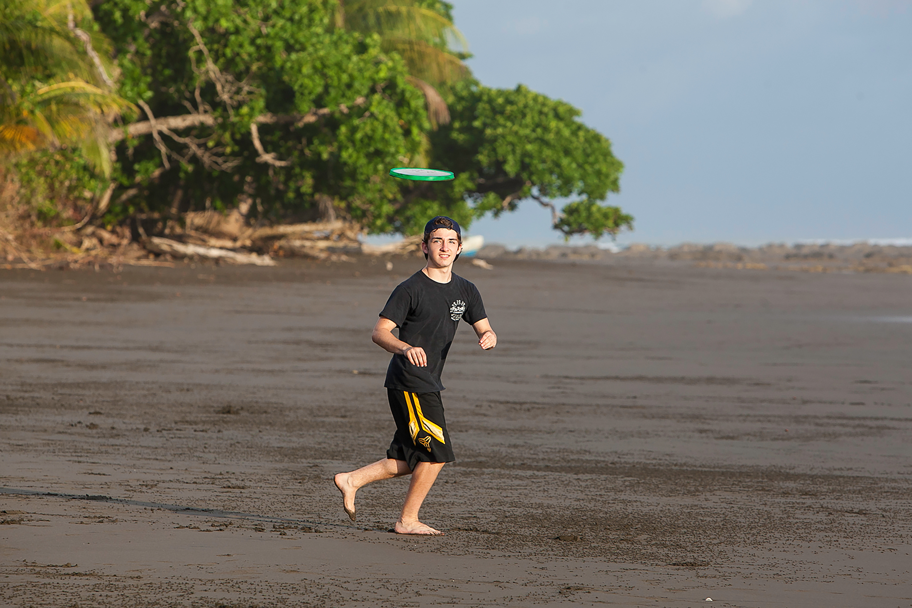 Person of boy running to catch a frisbee on the beach.