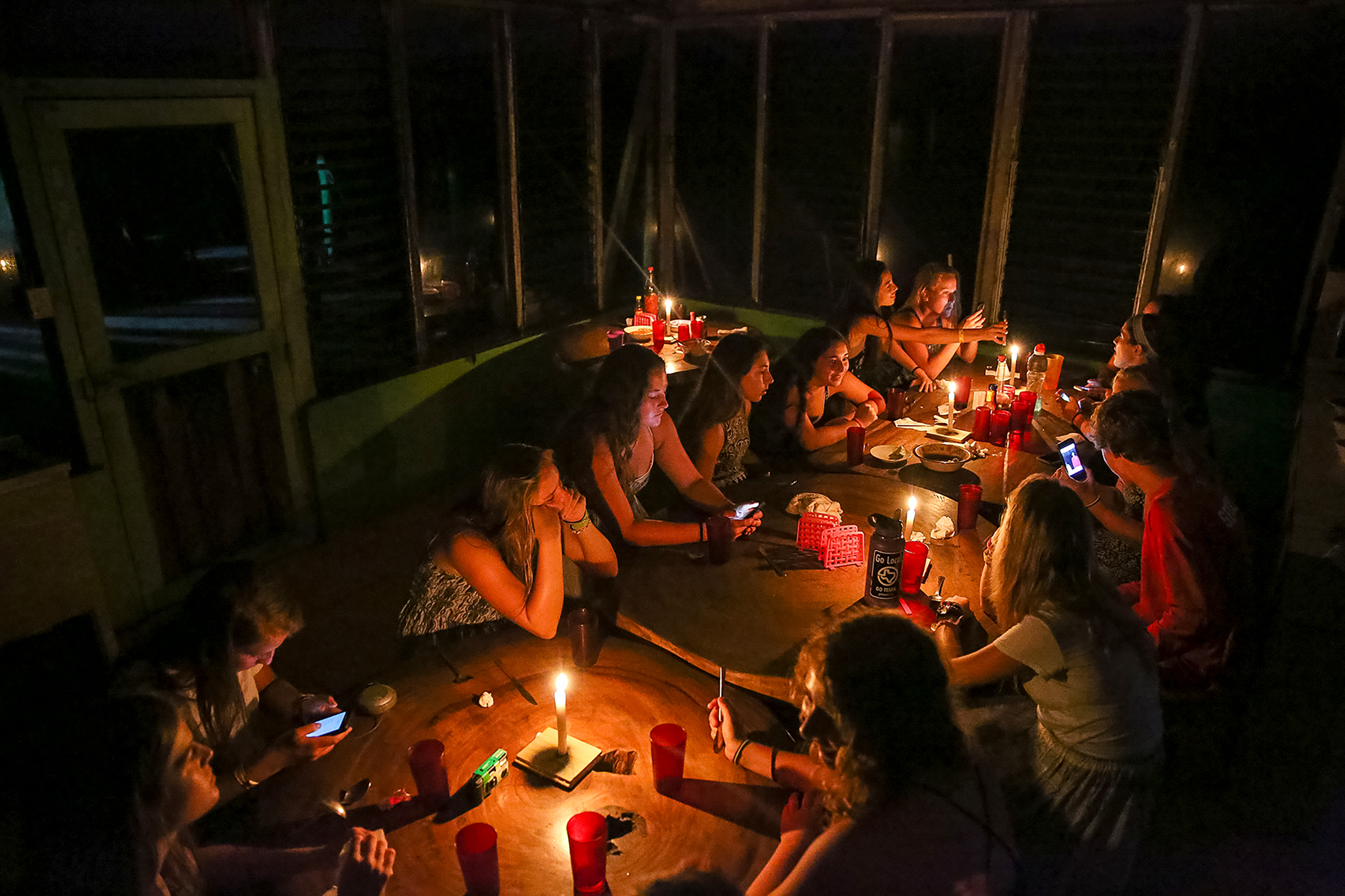 Picture of students sitting together at tables lit by candles and having a conversation during night time.