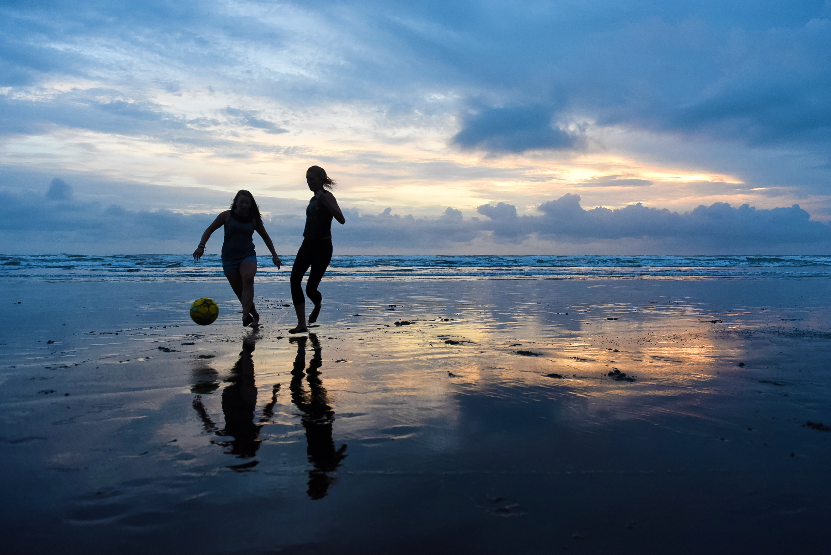 Students playing soccer during sunset at the beach.