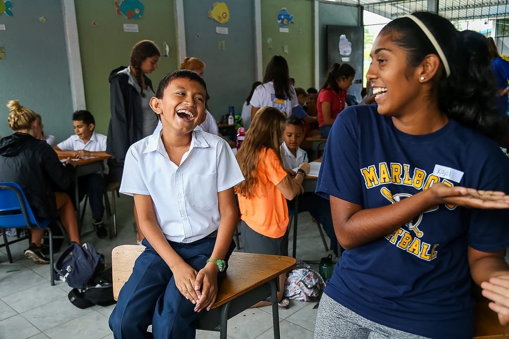 Child and a student volunteer laughing together in a classroom.
