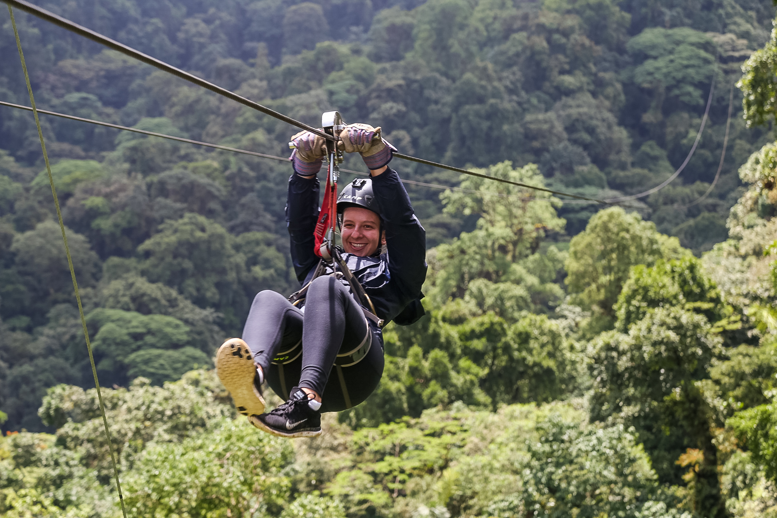 On a school trip, a student ziplines above a rainforest canopy
