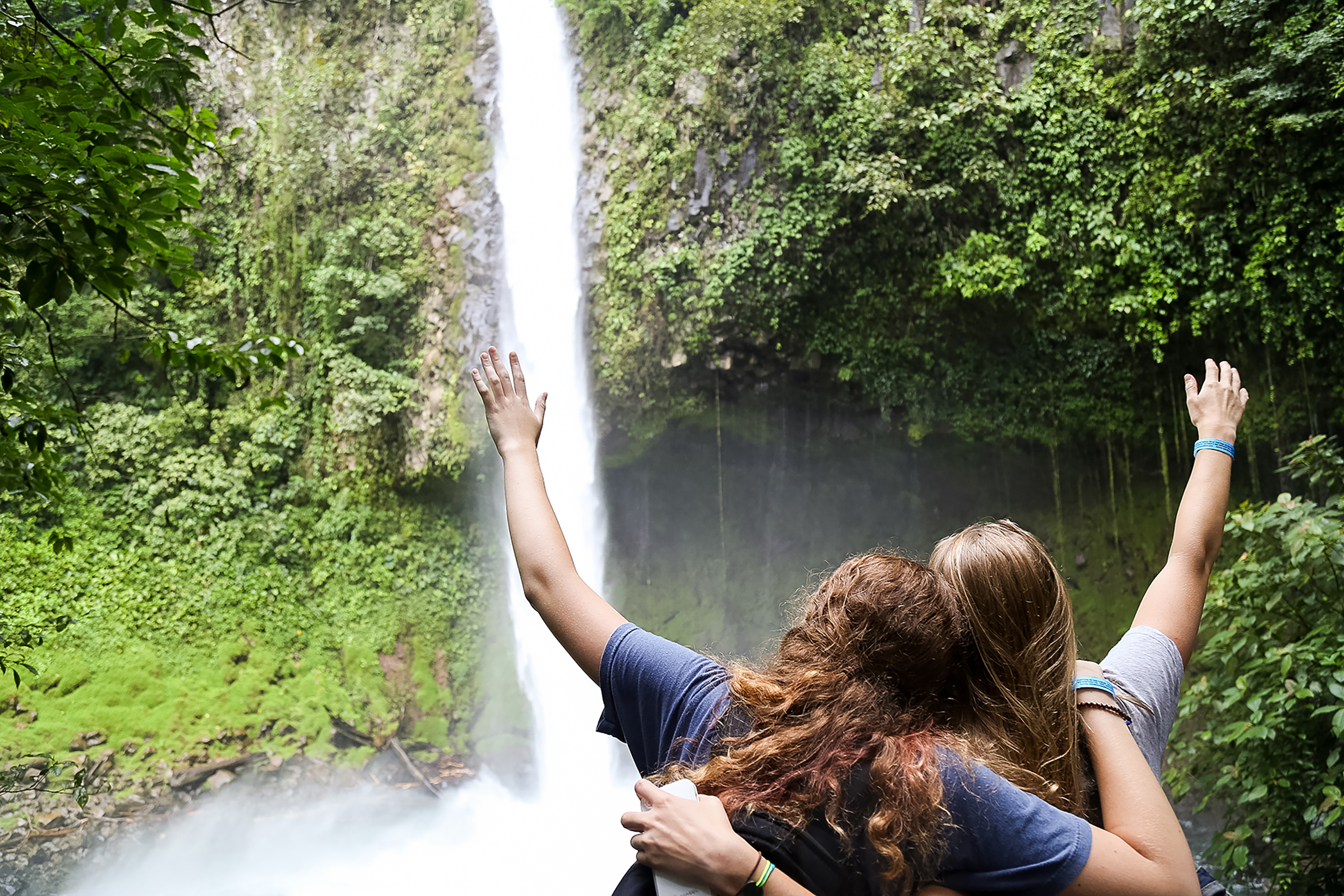 Students raise their arms toward a rainforest waterfall