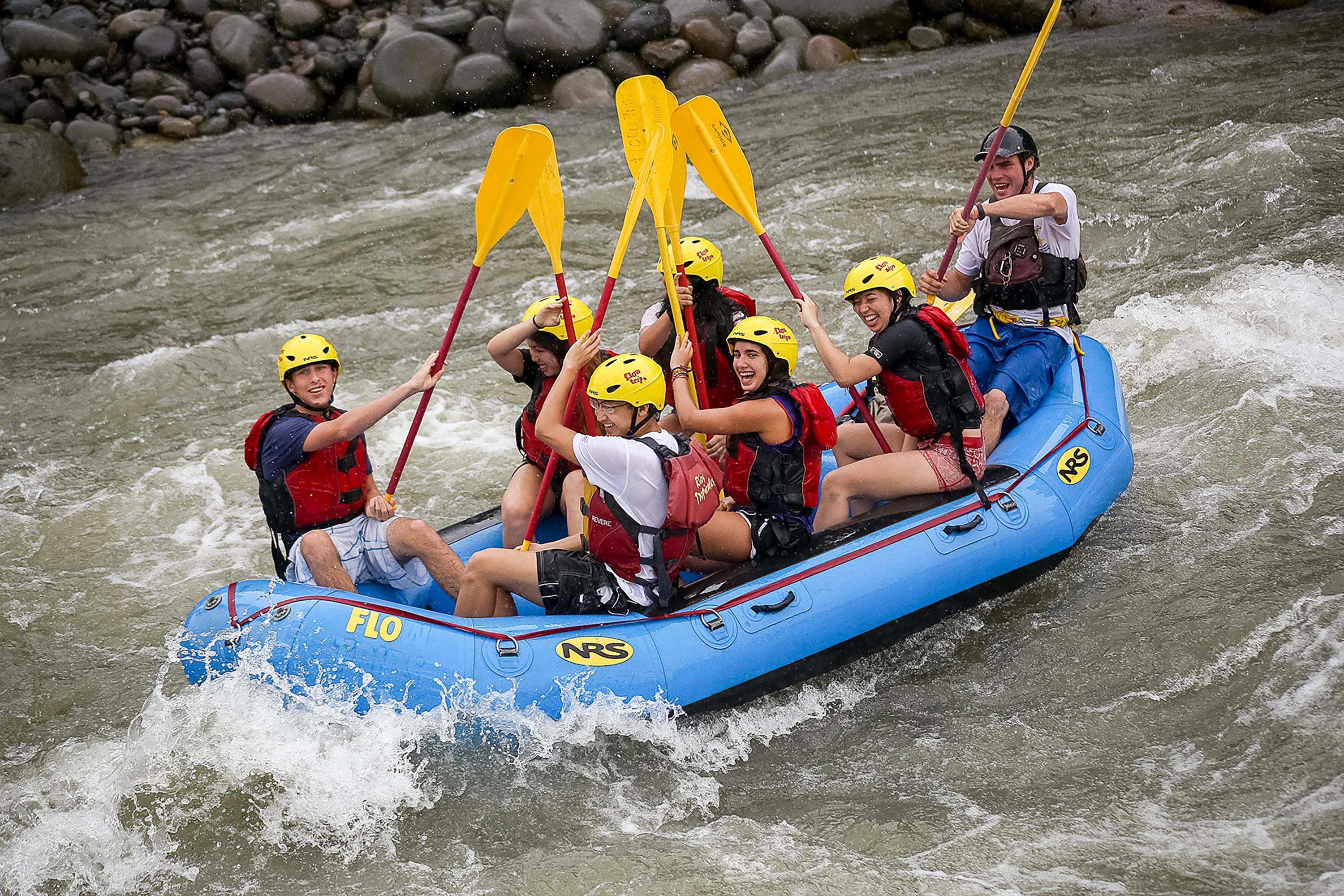 Students raise paddles while whitewater rafting through rapids