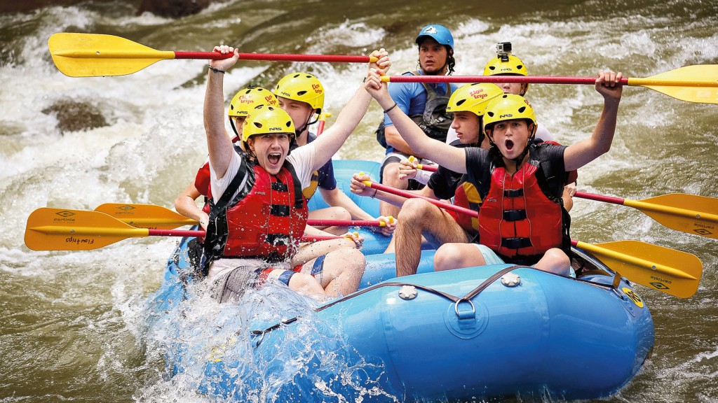 Students in helmets and life jackets cheer while whitewater rafting