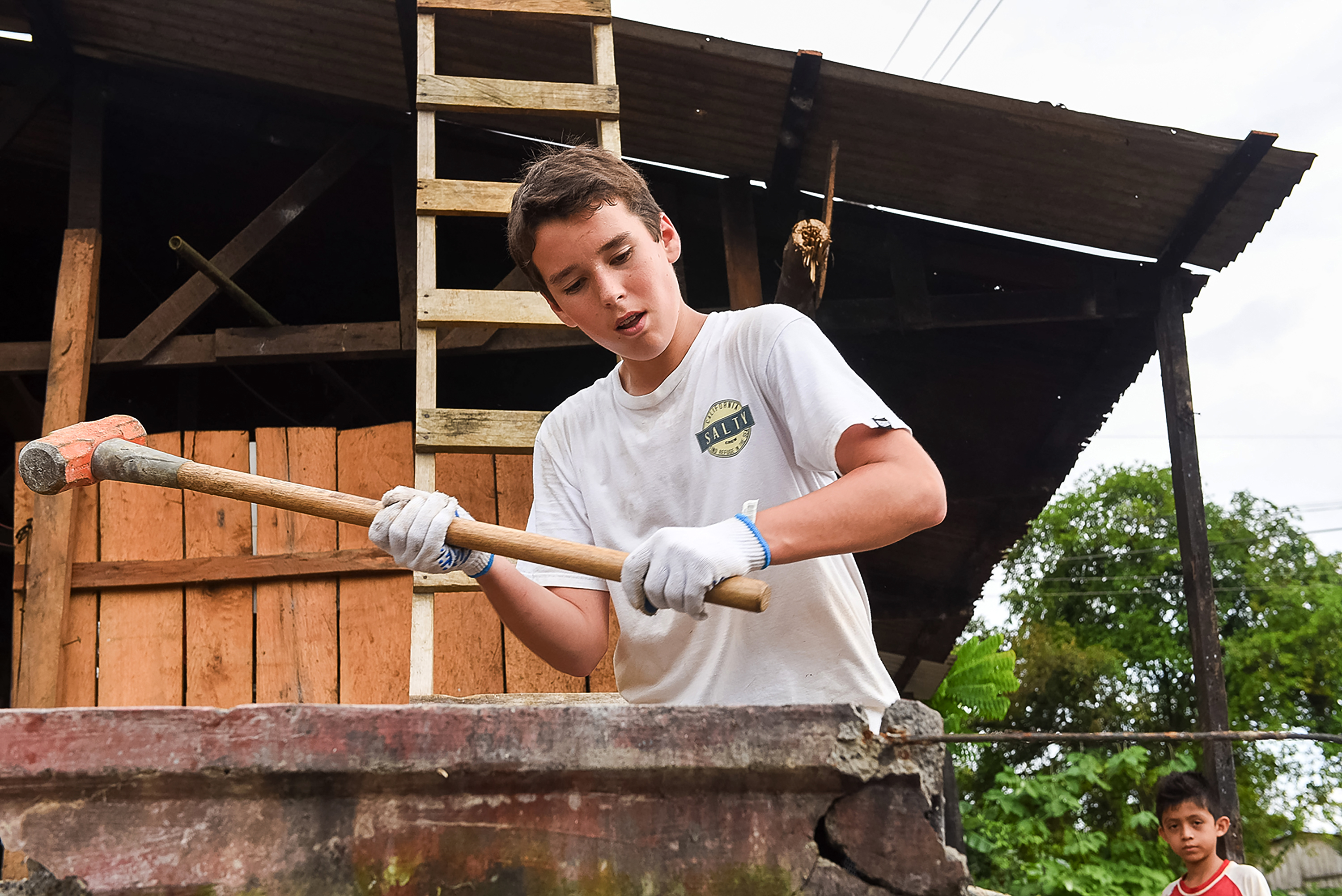 A student mixes concrete with a hoe during a community service project
