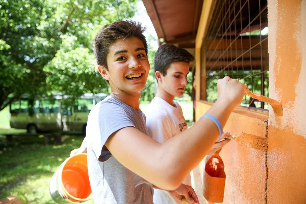 Two students paint a wall in orange.