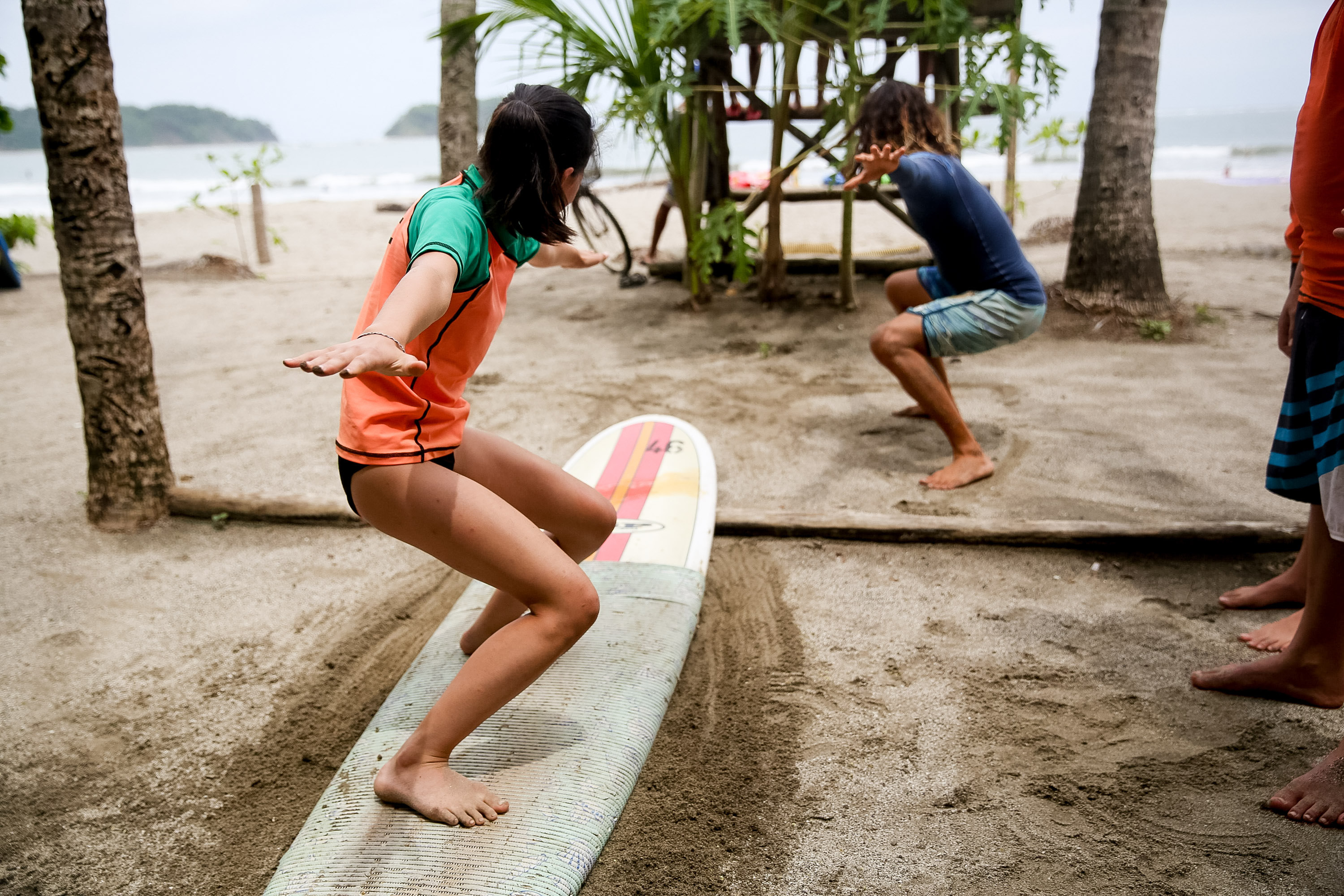 Students practice standing on surfboards set up in the sand for a surf lesson