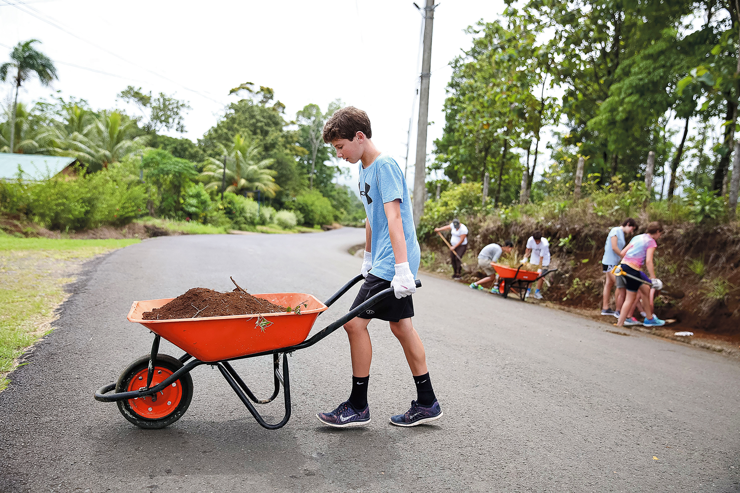 Students push a wheelbarrow of soil down a road during a service project