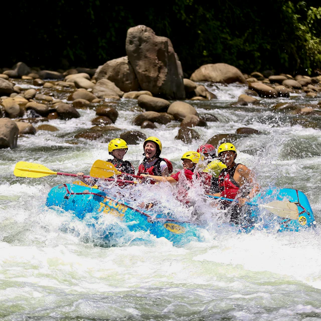 Students in yellow helmets and life vests paddle a blue raft through whitewater in Costa Rica