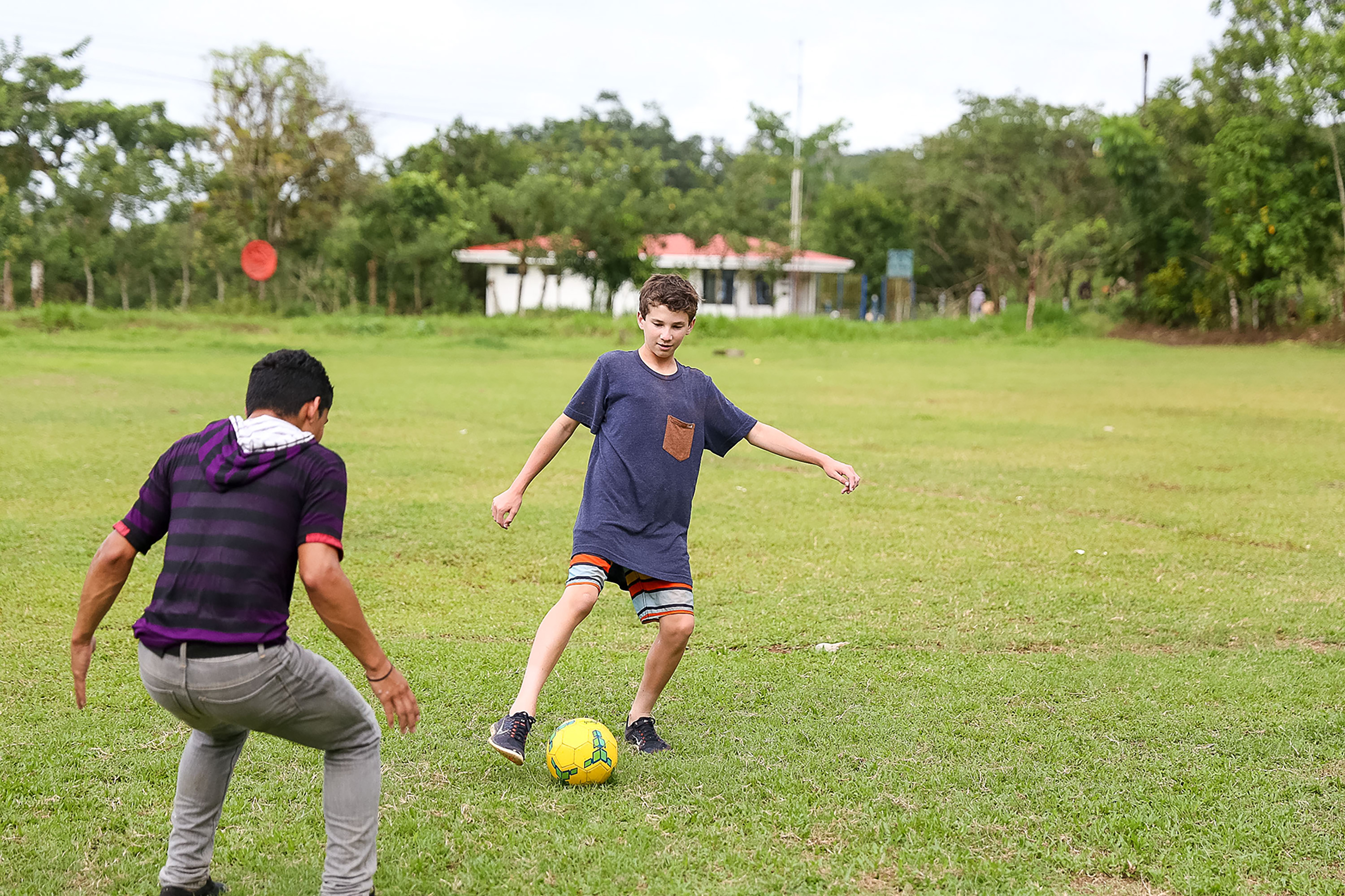 Students play soccer on a grassy field with a local player